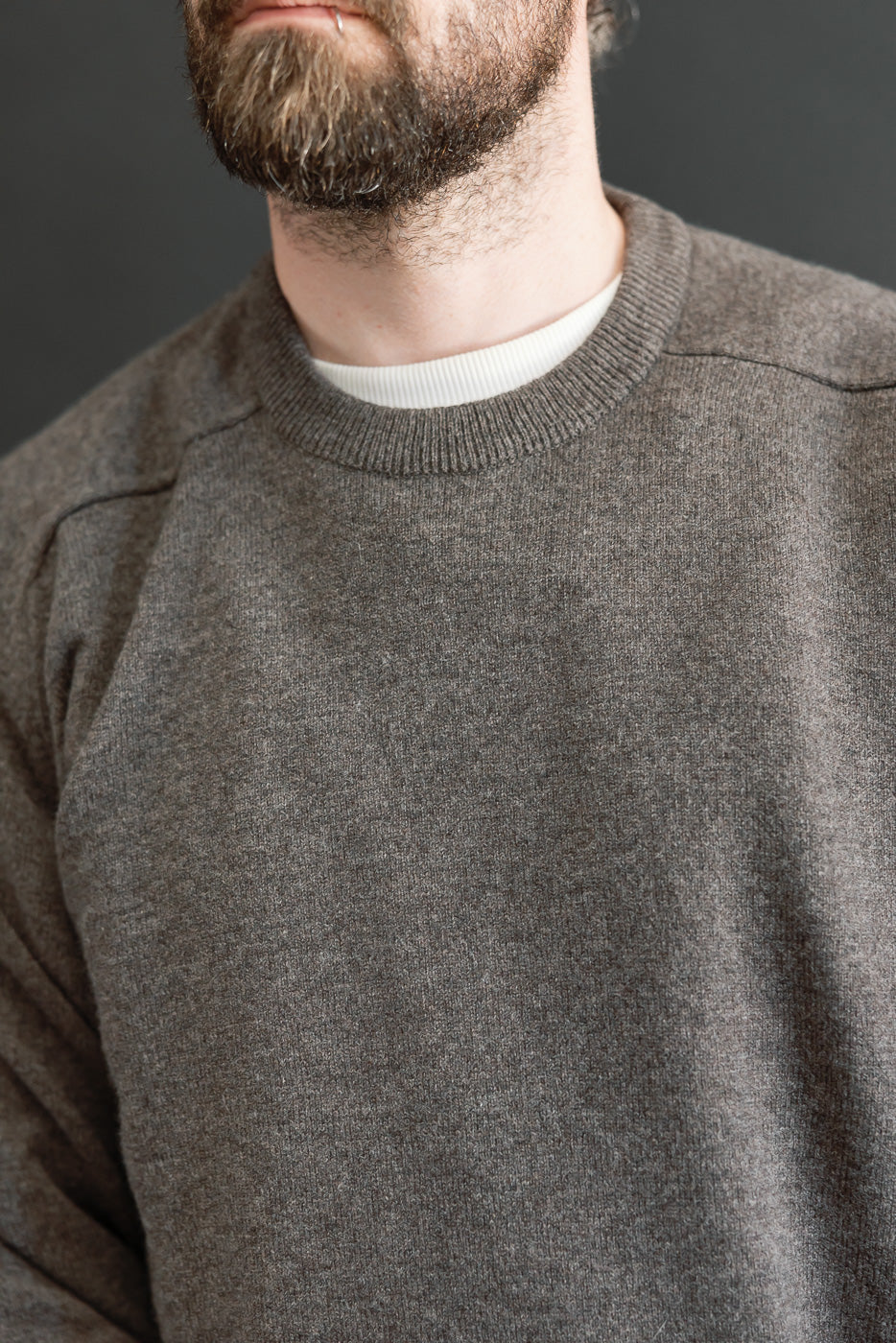 Close-up front view of a male model wearing a textured grey crewneck sweater over a white t-shirt.