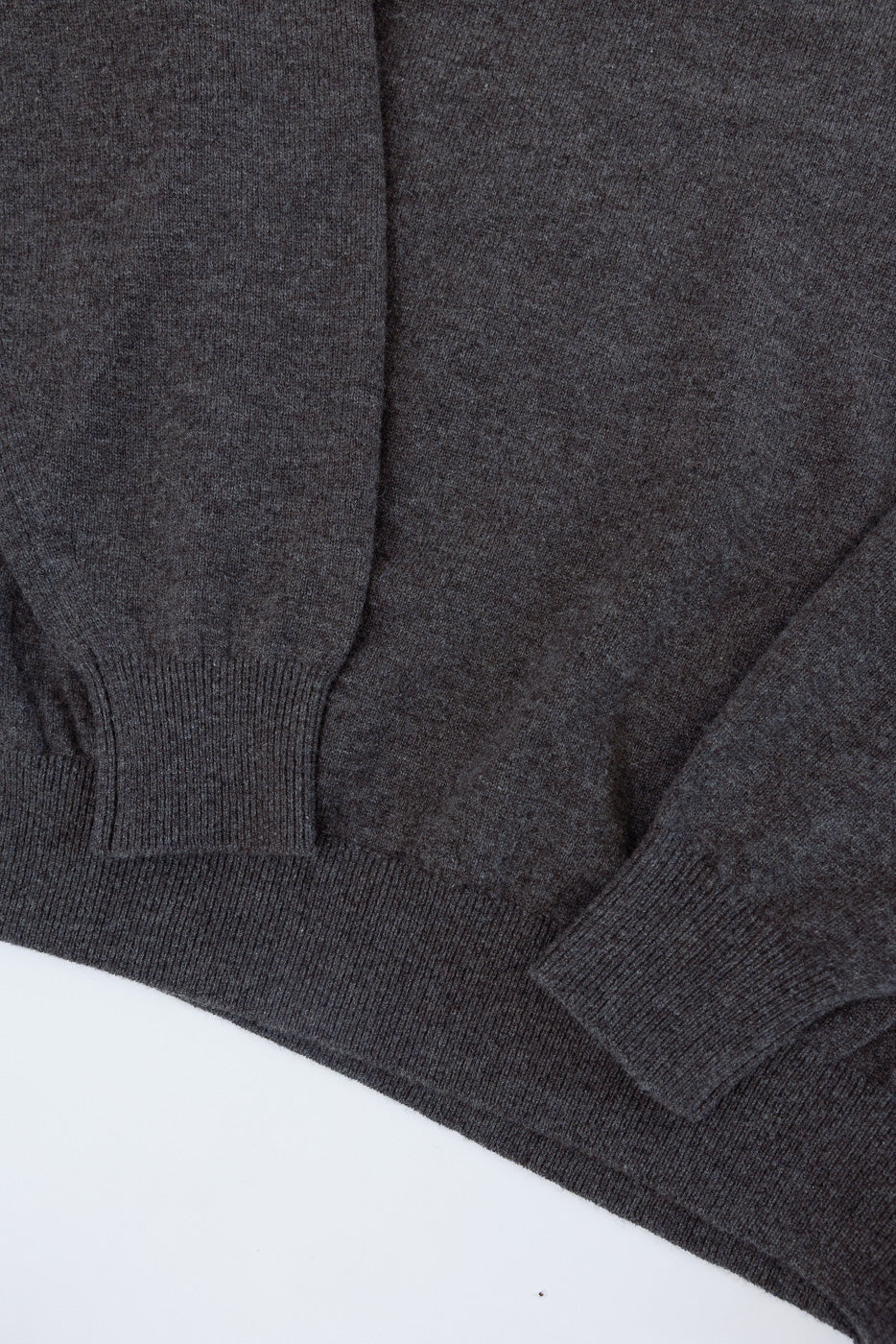 Close-up of the front bottom hem and left sleeve cuff of a charcoal grey knit sweater.