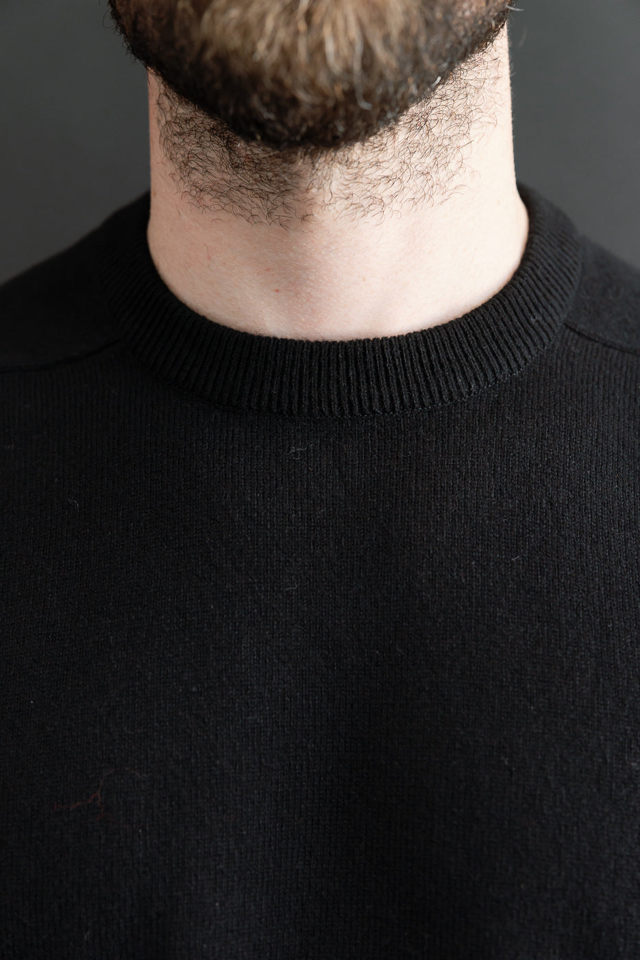 Close-up of the ribbed crewneck collar and fine knit texture of a black sweater.