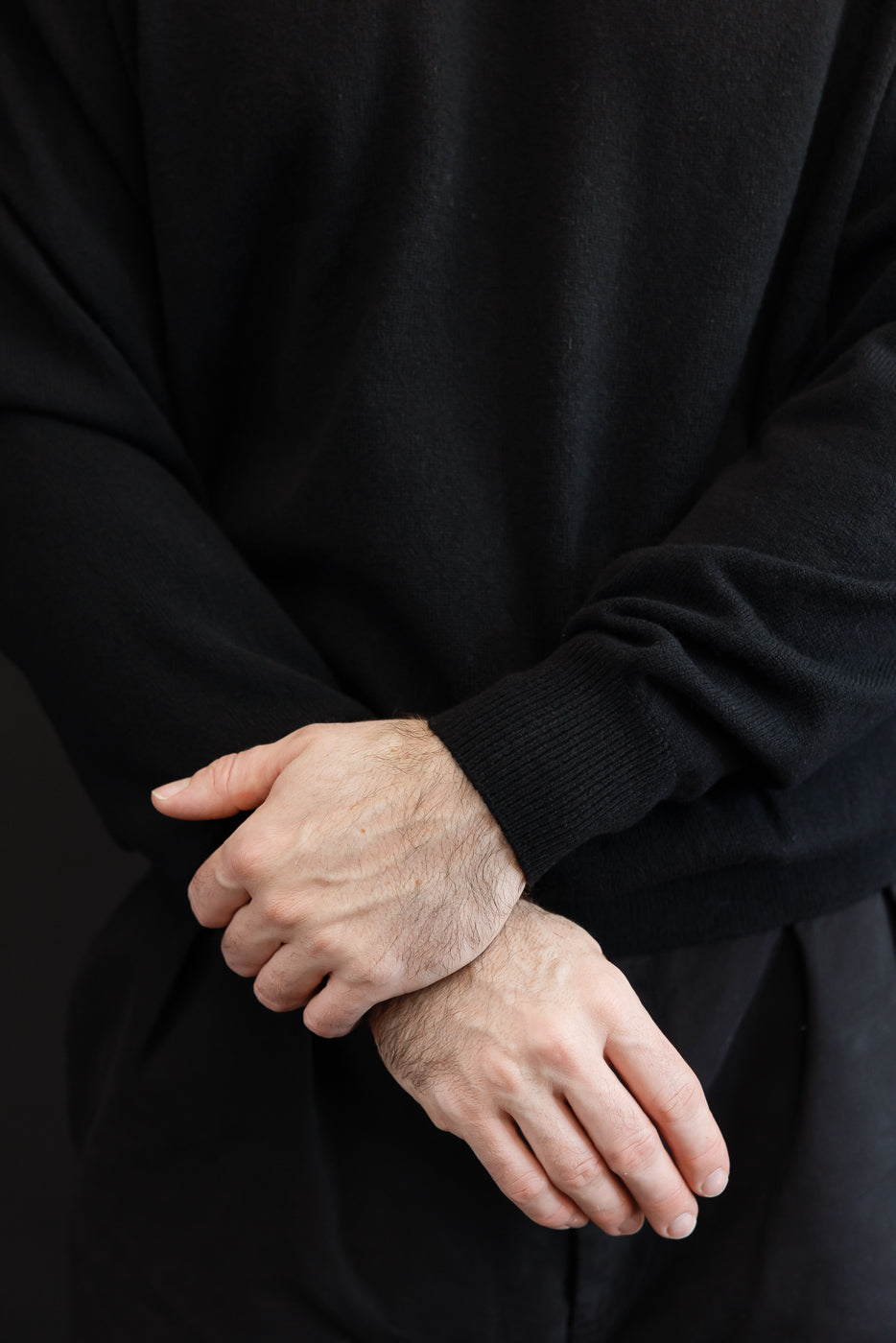 Close-up of the sleeve and cuff of a black long-sleeve shirt on a male model.