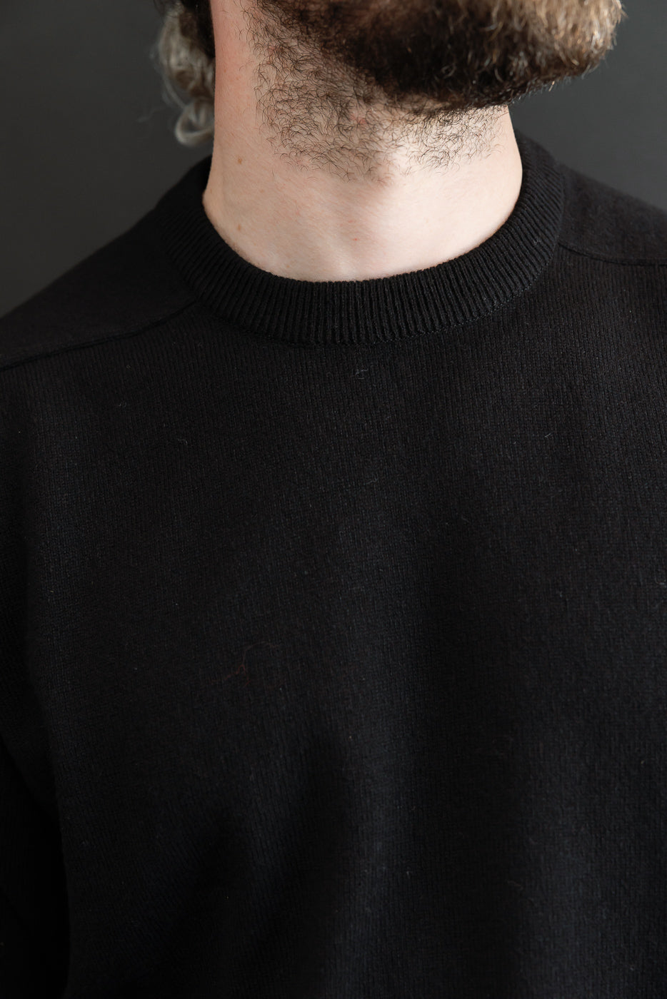 Close-up front view of a black crewneck sweater on a male model, 5'9