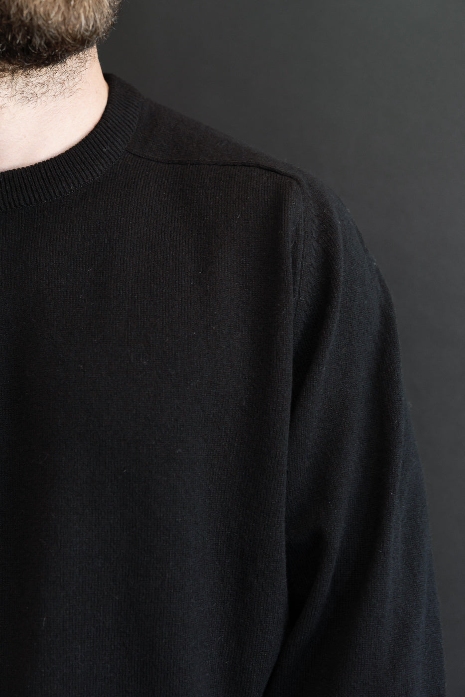 Close-up of the front shoulder and neckline of a black crewneck sweater on a male model.