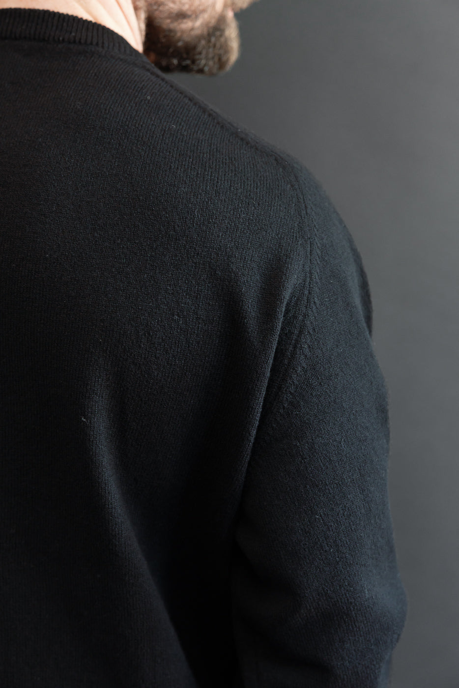 Close-up of the back and right shoulder of a black knit sweater showing fine fabric texture.