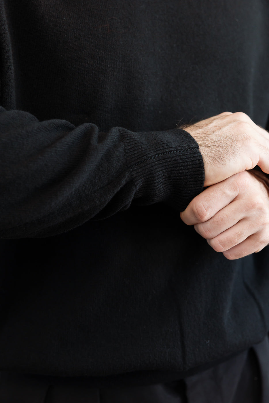 Close-up of the sleeve and cuff of a male model's black sweater, showing fabric texture.