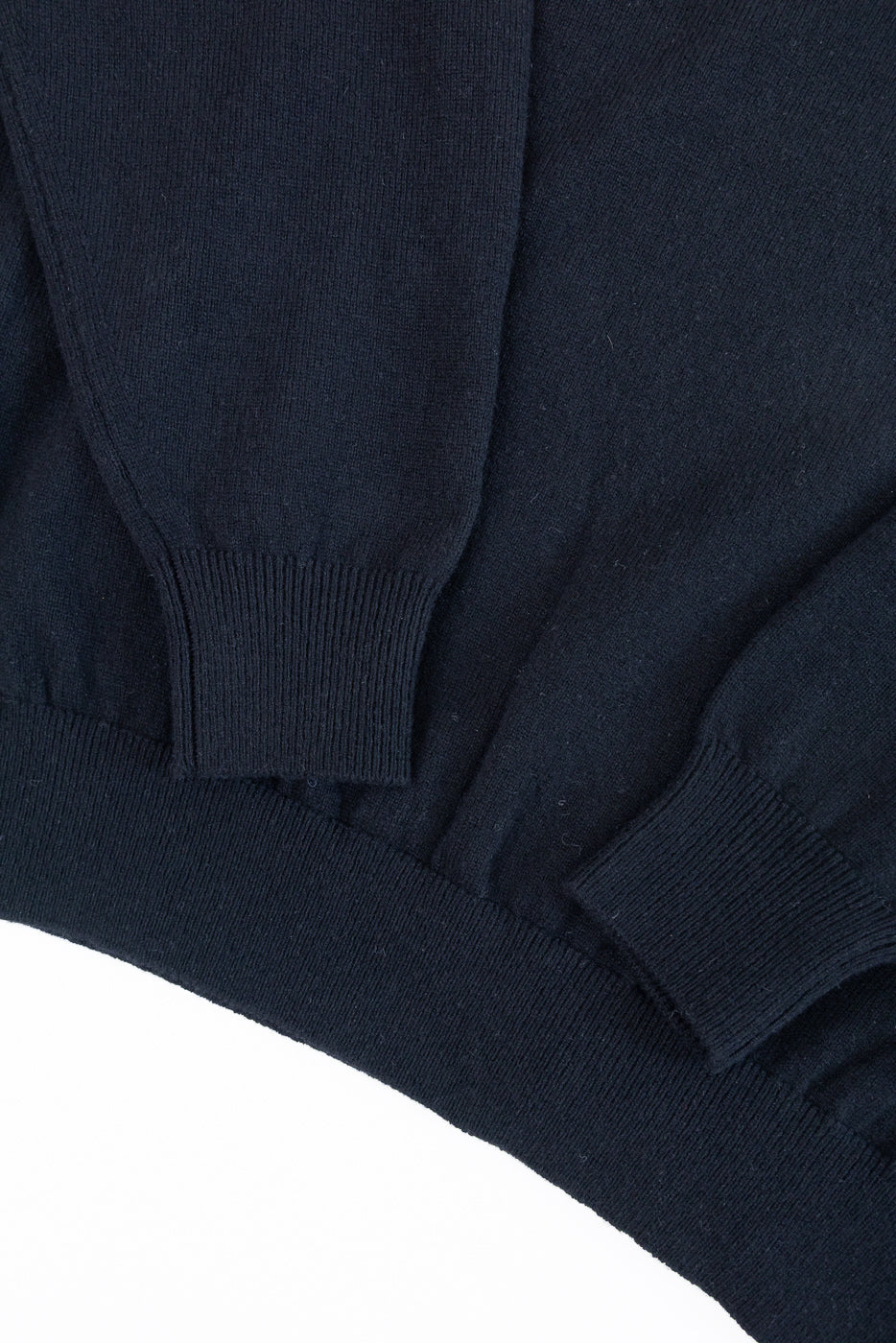 Close-up of the ribbed cuffs and hem of a navy blue knit sweater.