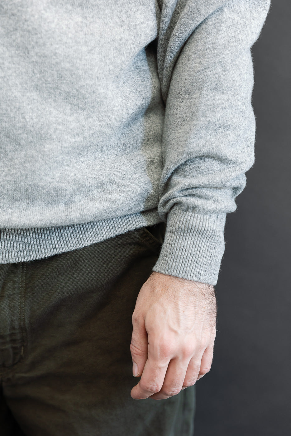Close-up of the front side of a grey knit sweater hem and ribbed cuff on a male model.
