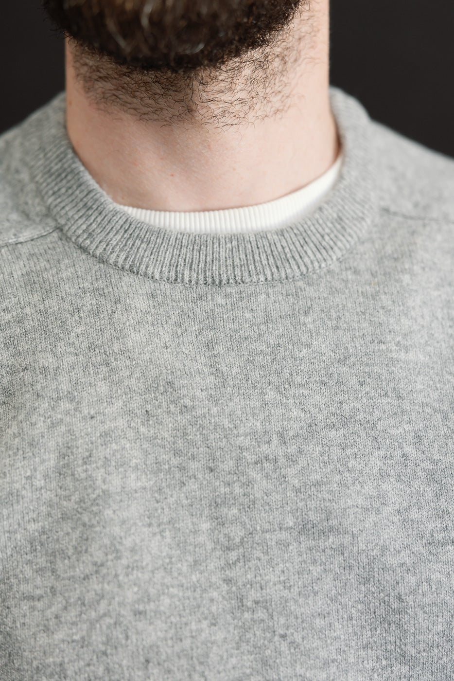 Close-up front view of a grey crewneck sweatshirt's ribbed collar and fabric texture on a male model.