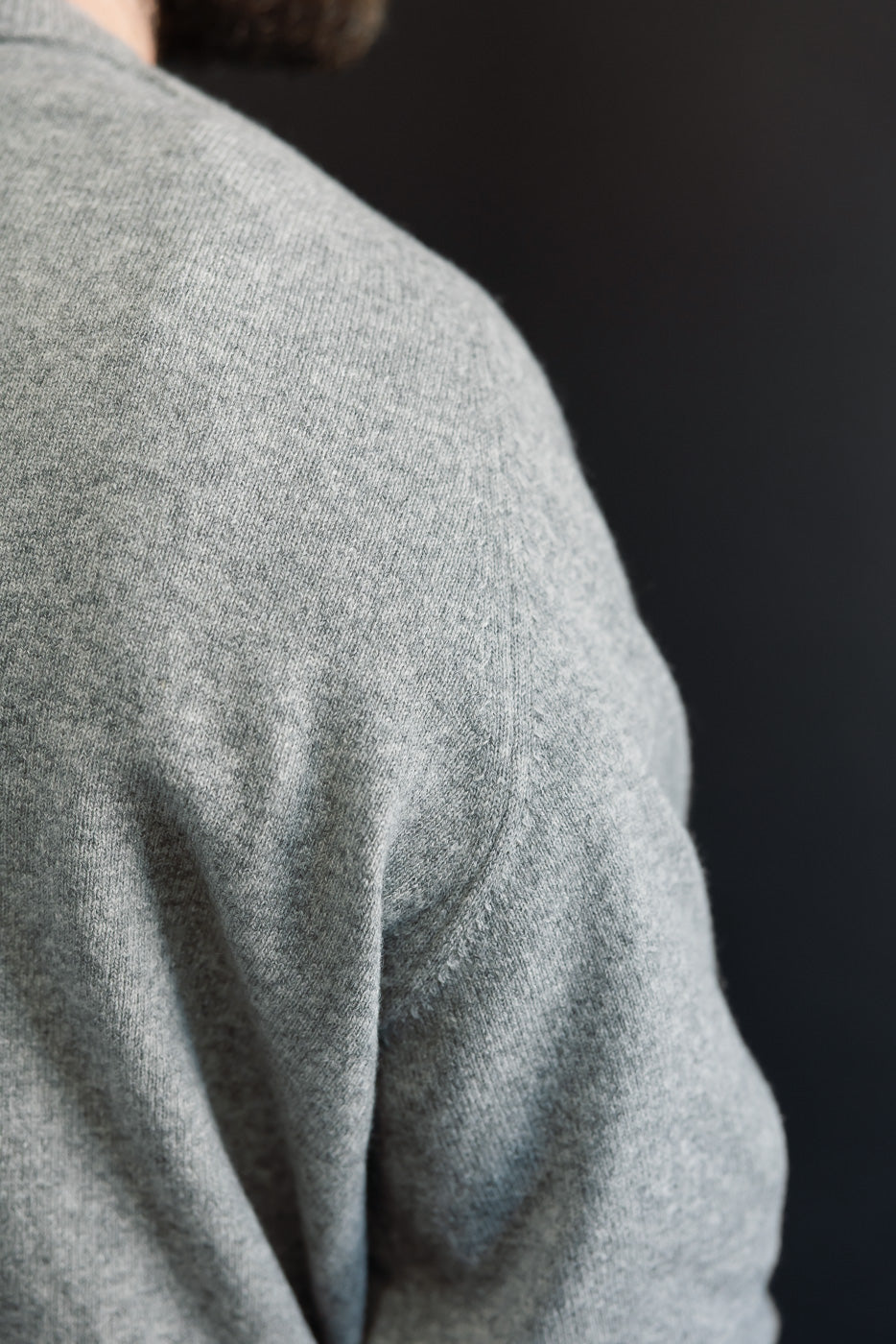 Close-up of the right shoulder and sleeve texture on a grey knit sweater worn by a male model.