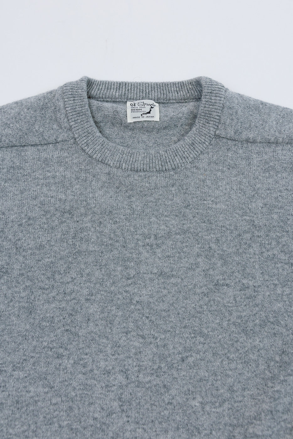 Close-up front view of a grey sweater neckline featuring a ribbed collar and interior tag.