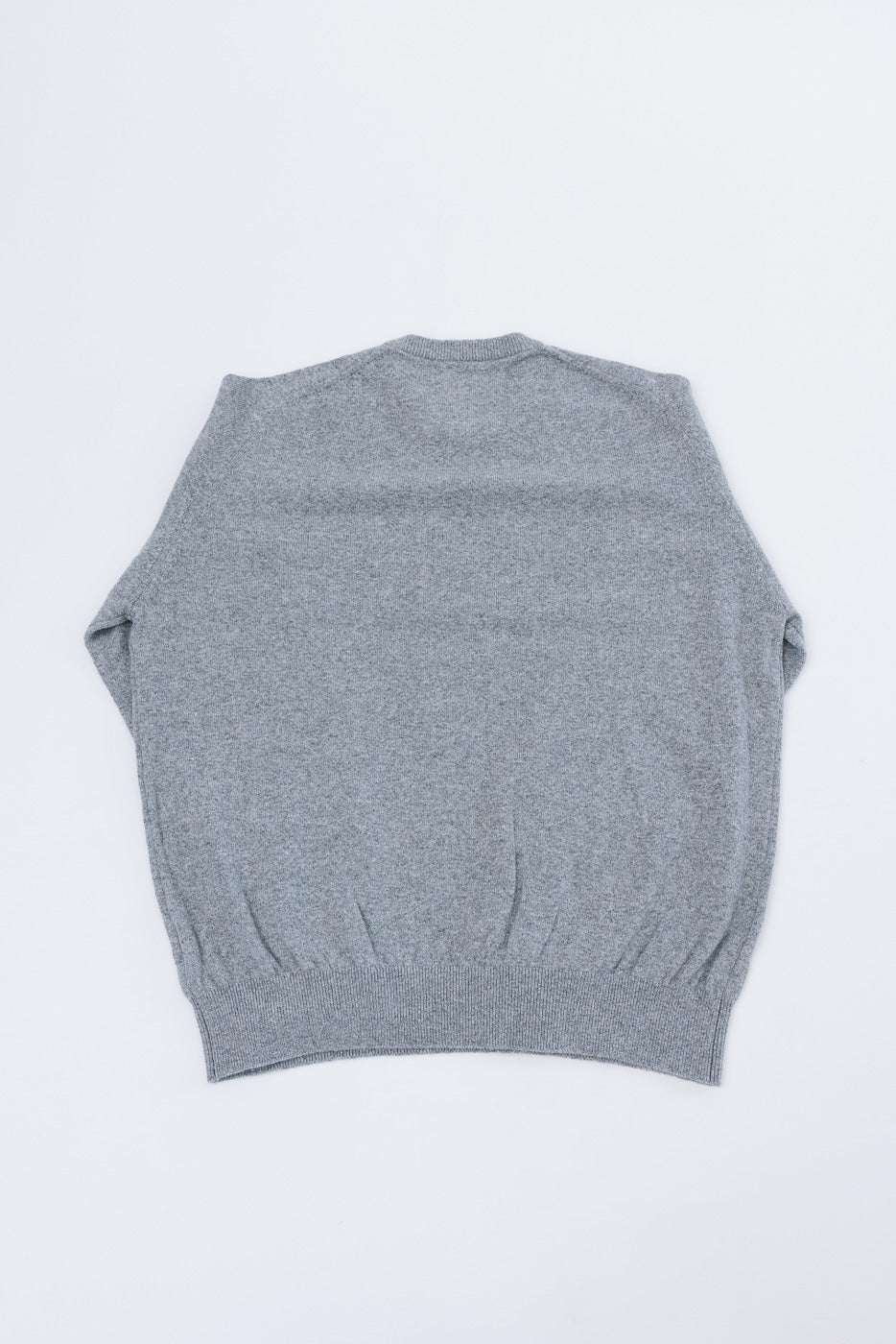 Flat lay, back view of a grey knit sweater showing the rear hem and shoulder construction.