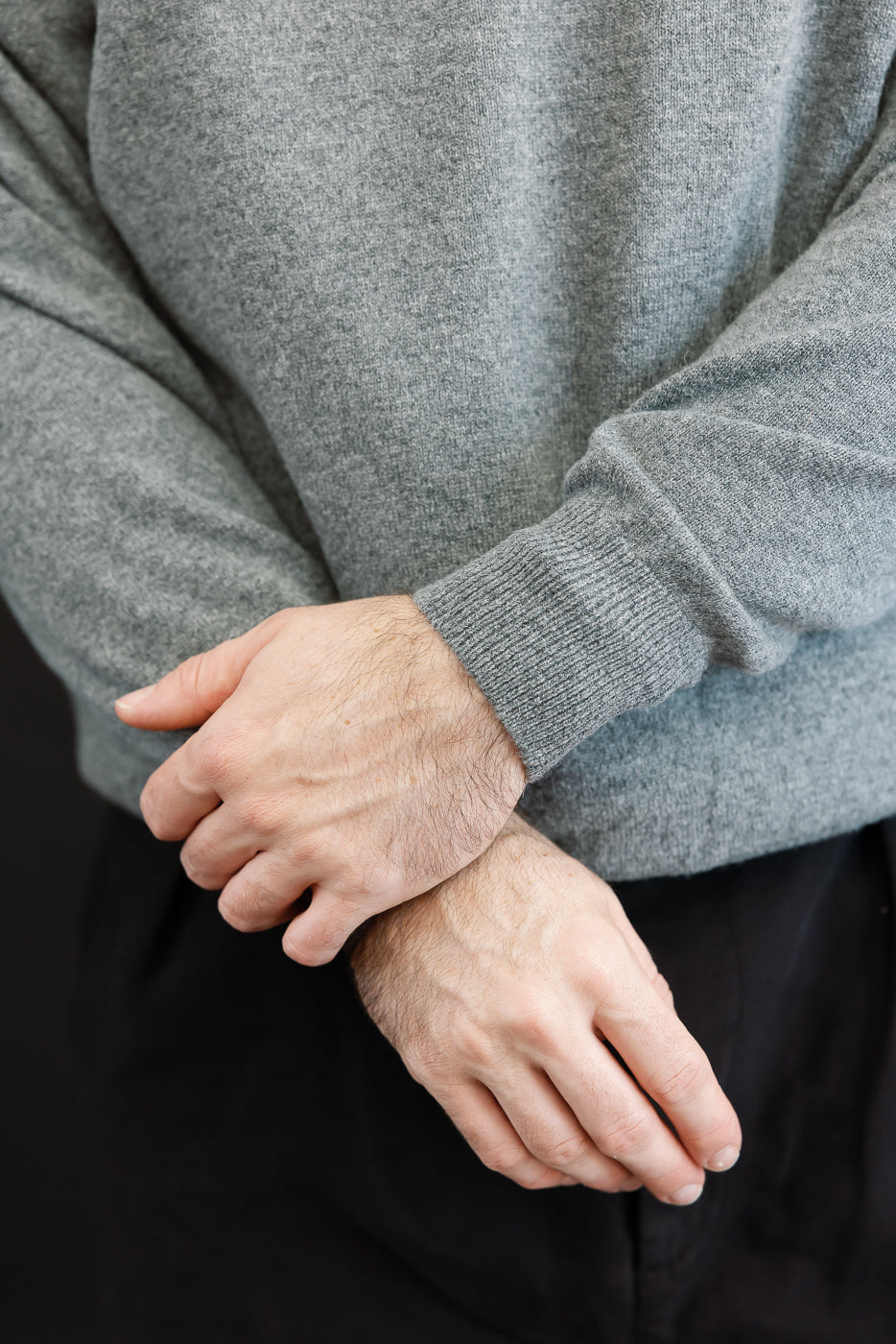 Close-up of the front texture and ribbed cuffs of a grey crewneck sweater worn by a male model.