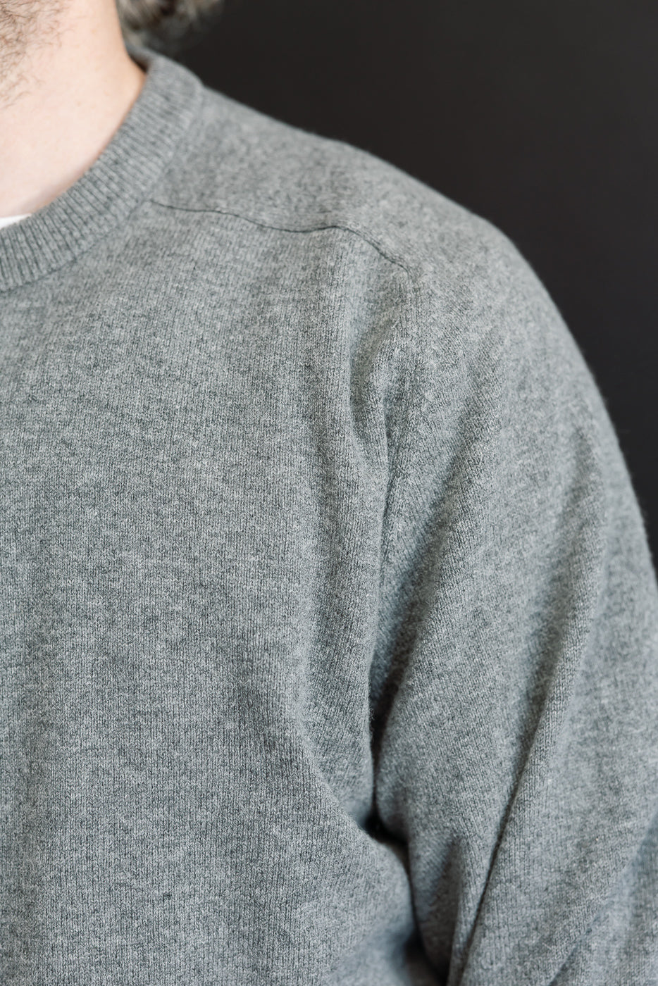 Close-up of the front shoulder and neckline of a grey crewneck sweater showing fabric texture.