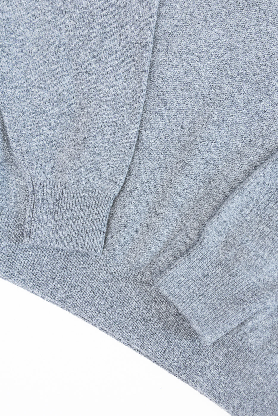 Close-up of a grey knit sweater's front hem and ribbed cuff, showing fabric texture.