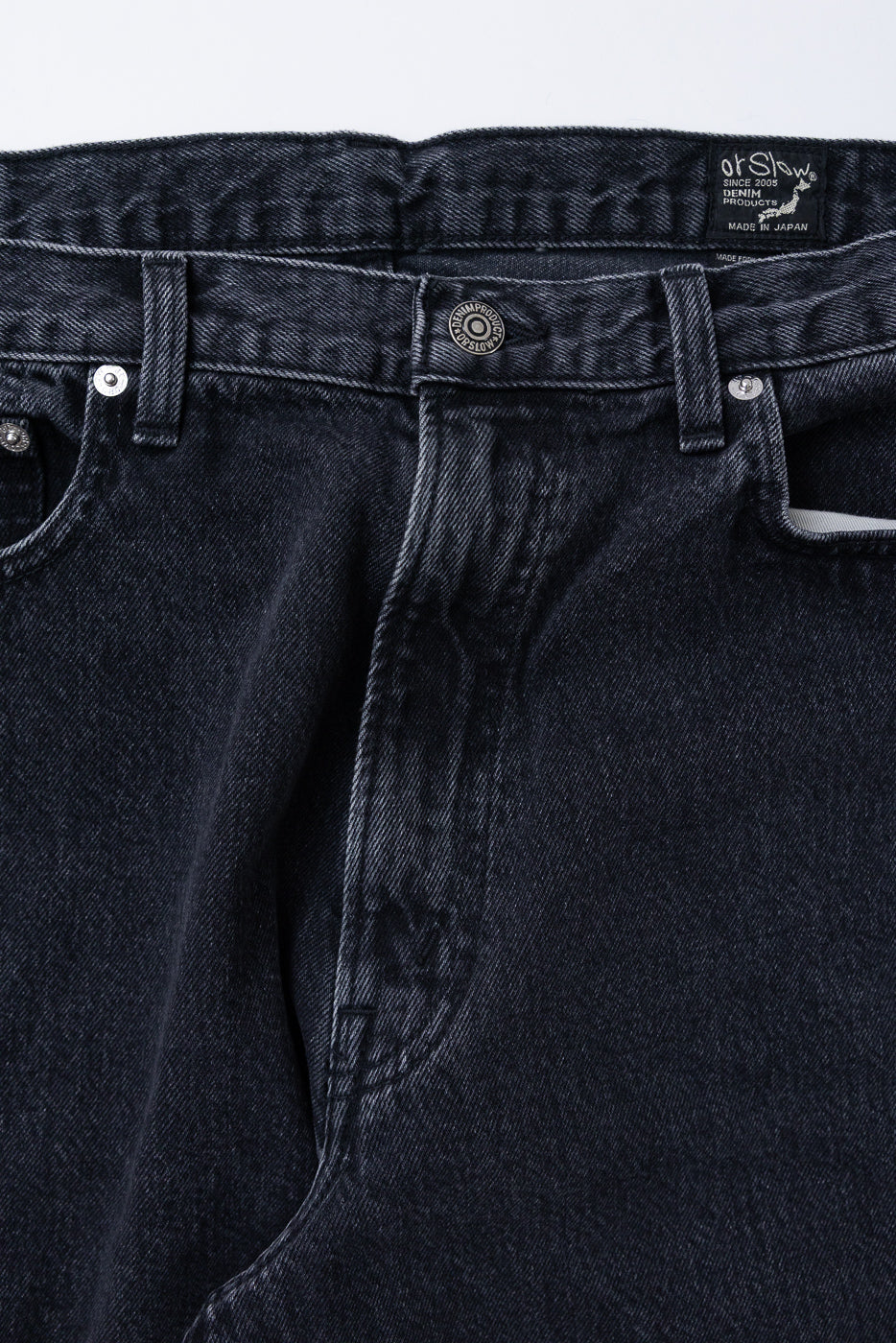 Close-up front view of black denim jeans showing waistband, button, and fabric texture.