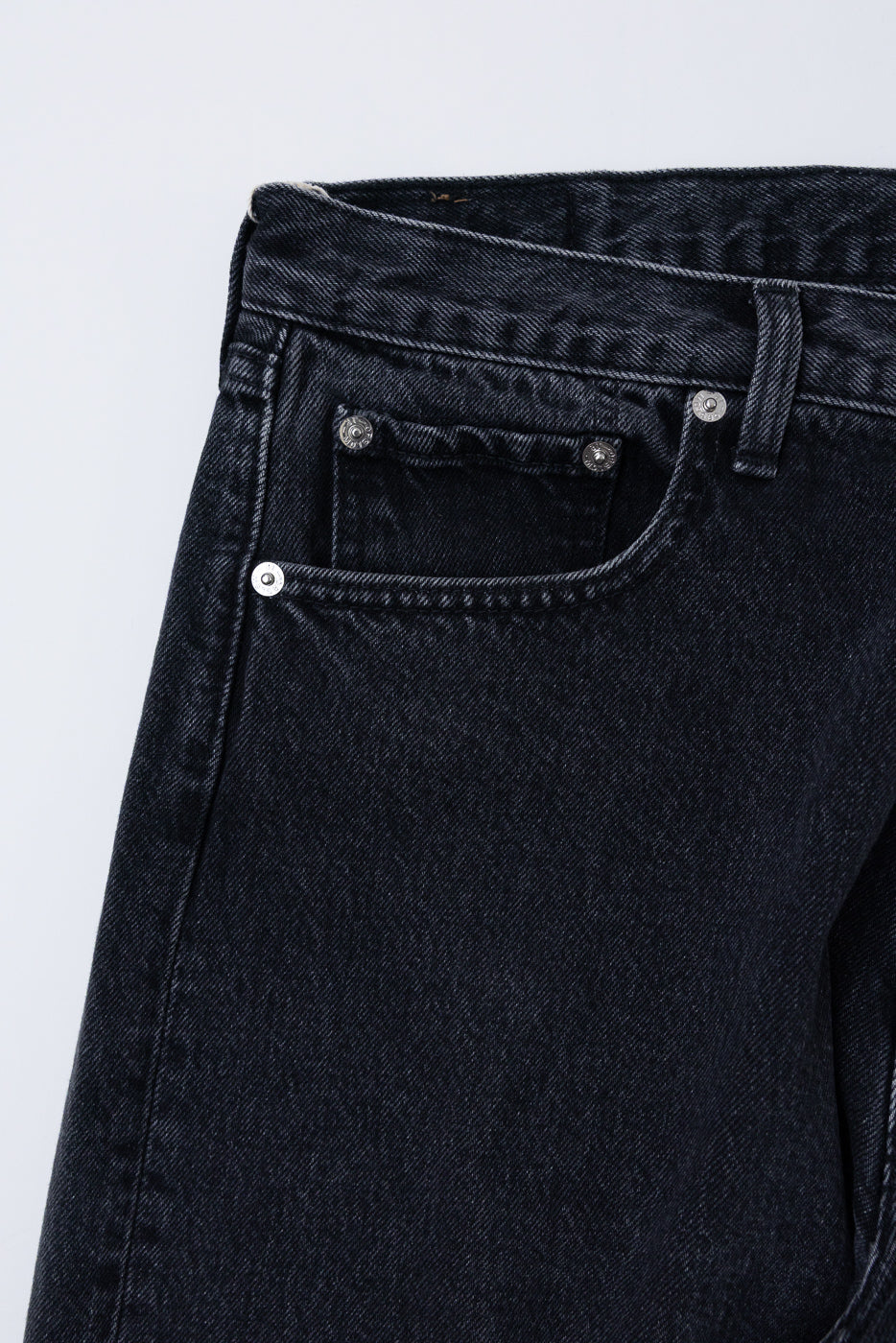 Close-up front view of black denim jeans showing waistband, belt loop, and coin pocket detail.