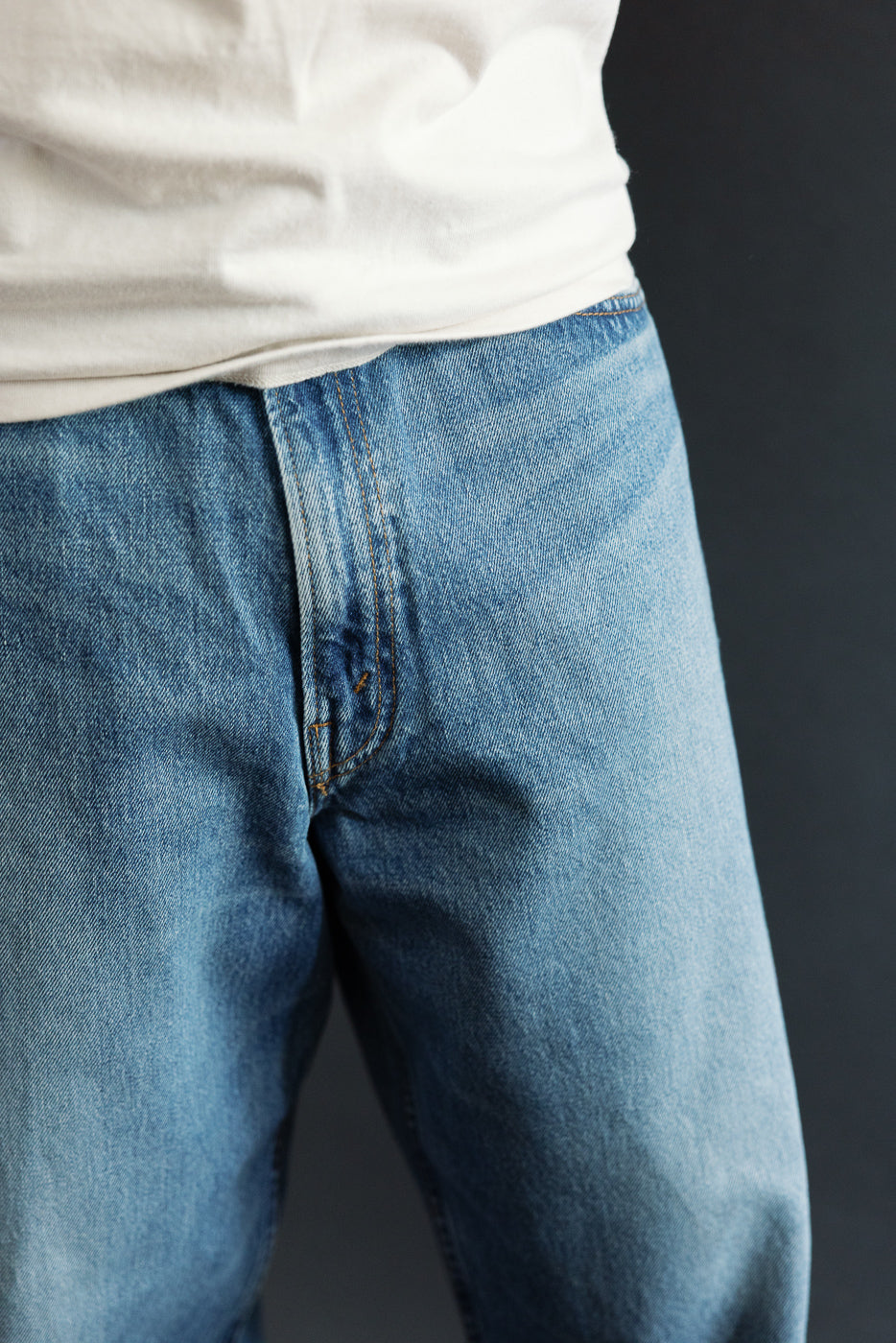 Close-up front view of men's selvedge denim jeans, showing fly detail and orange stitching on athletic build model