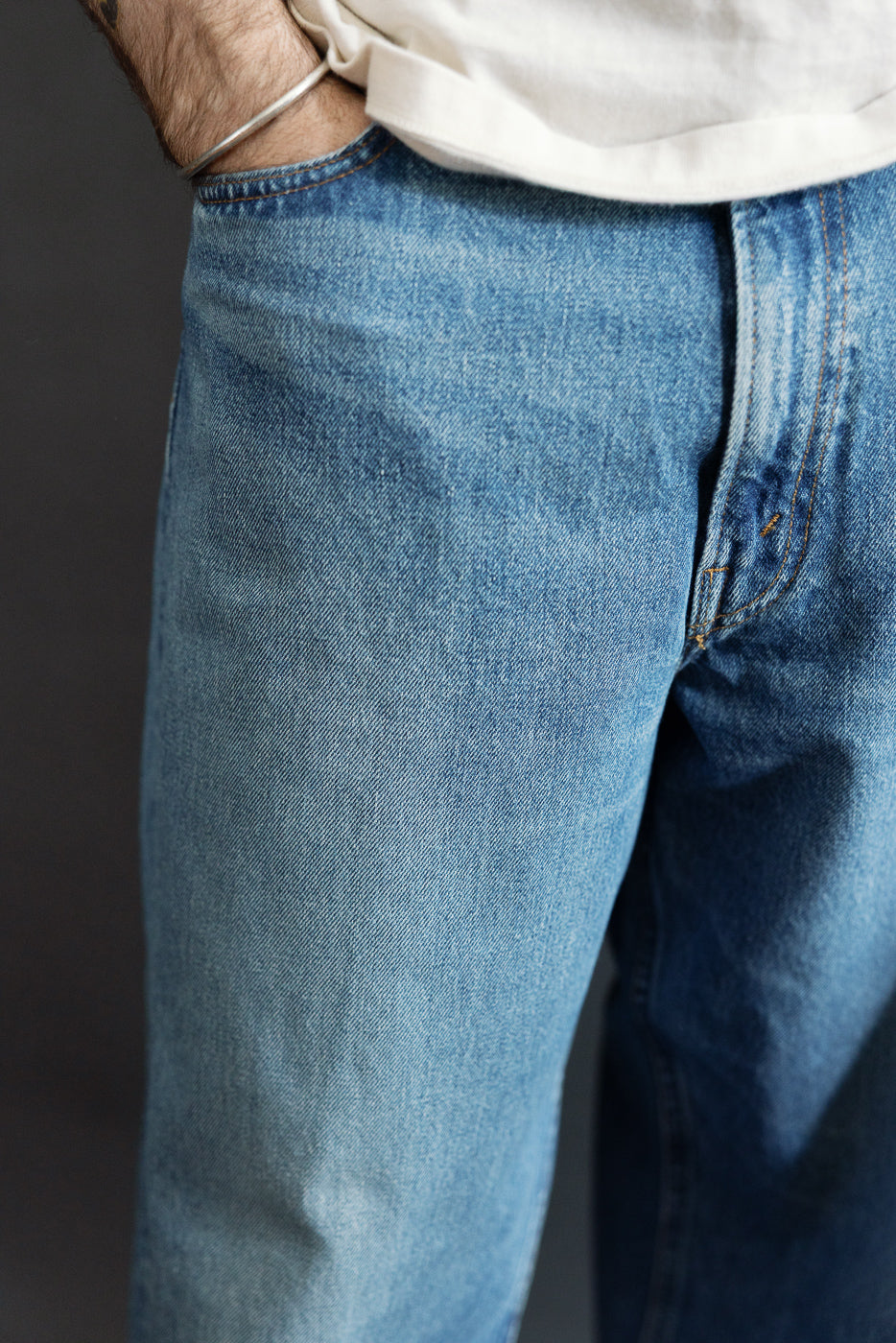 Close-up front view of men's selvedge denim jeans, showcasing fabric texture and orange stitching, worn by athletic male model