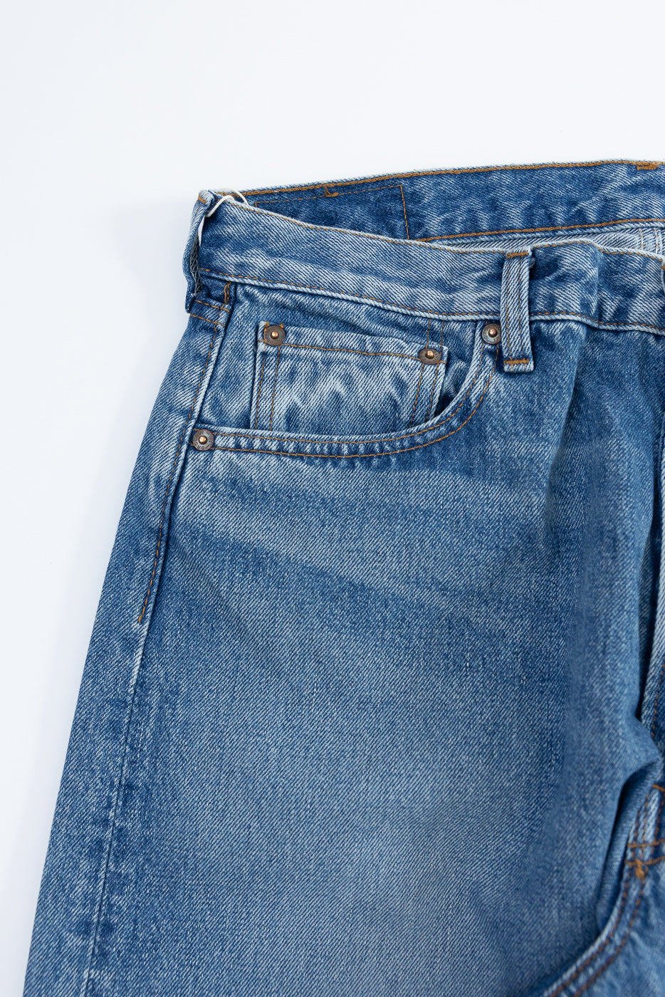 Close-up front view of men's selvedge denim jeans, showing waistband, button fly, and front pocket details