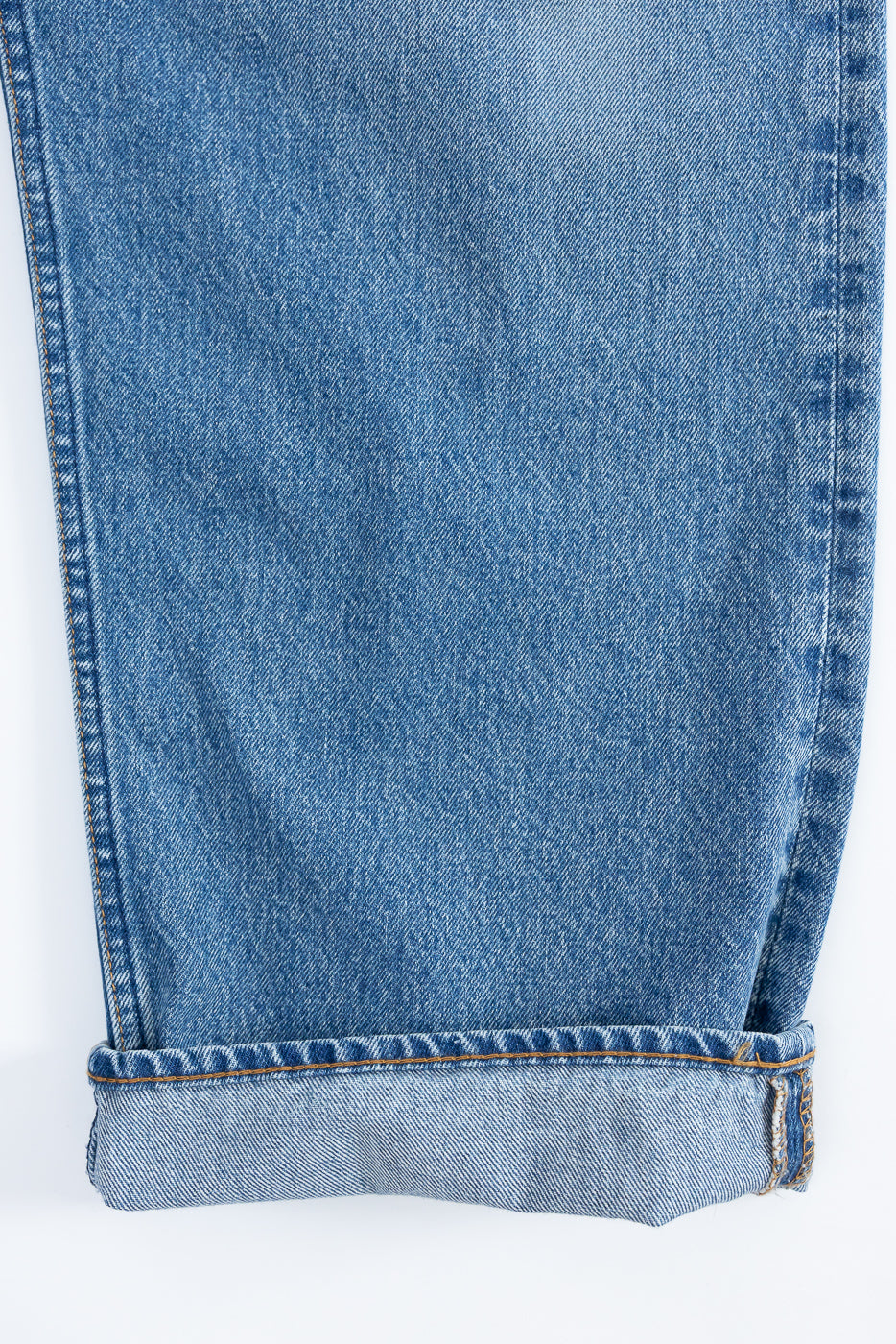 Close-up of men's selvedge denim jeans leg, front view, showing cuffed hem and orange stitching detail