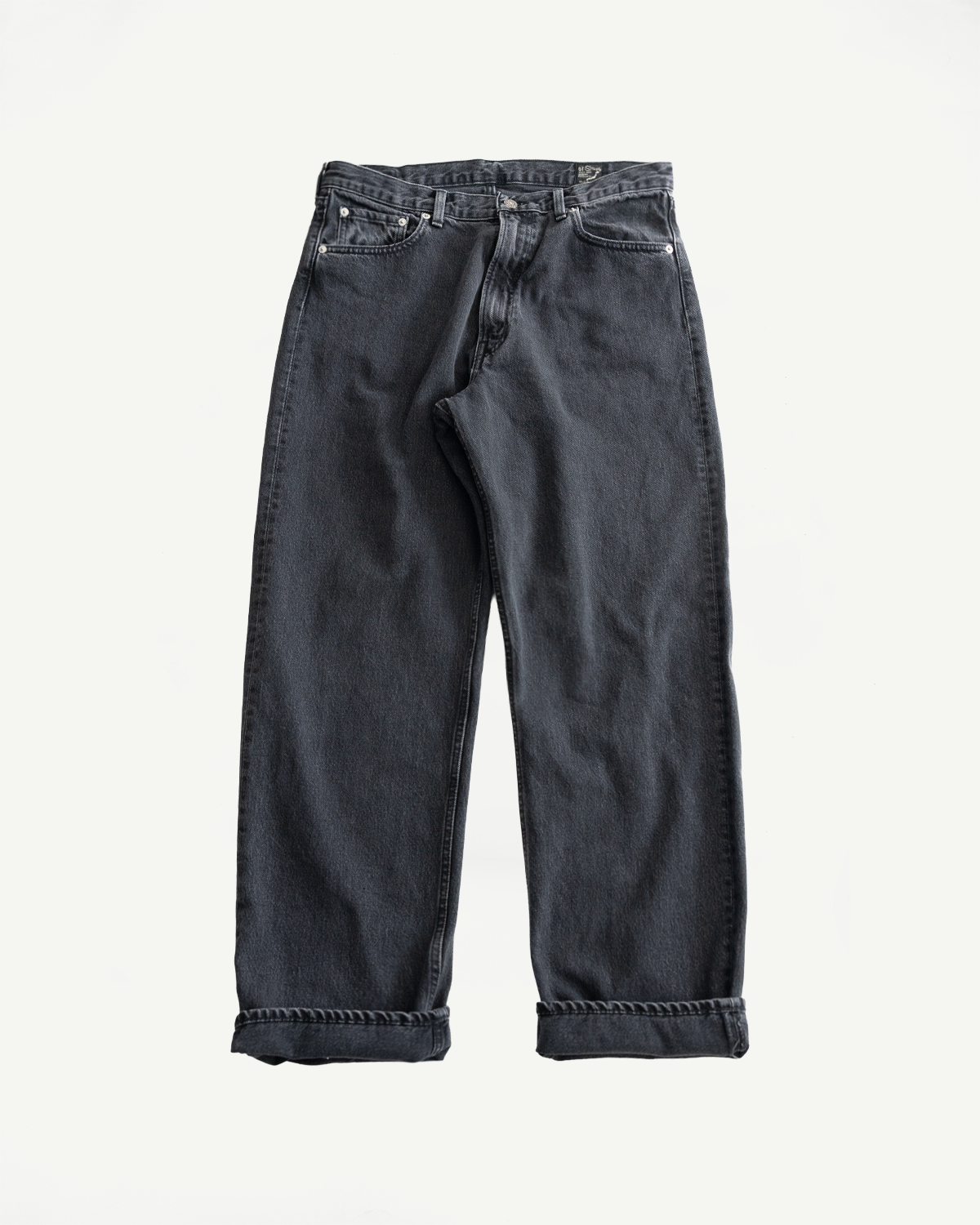 01-1010W-D61S - 101 Dad’s Fit Denim - 90s Black Stone jeans laid flat, showcasing their relaxed fit, five-pocket design, and straight legs. The stone-washed black denim features subtle grey tones for a vintage look.