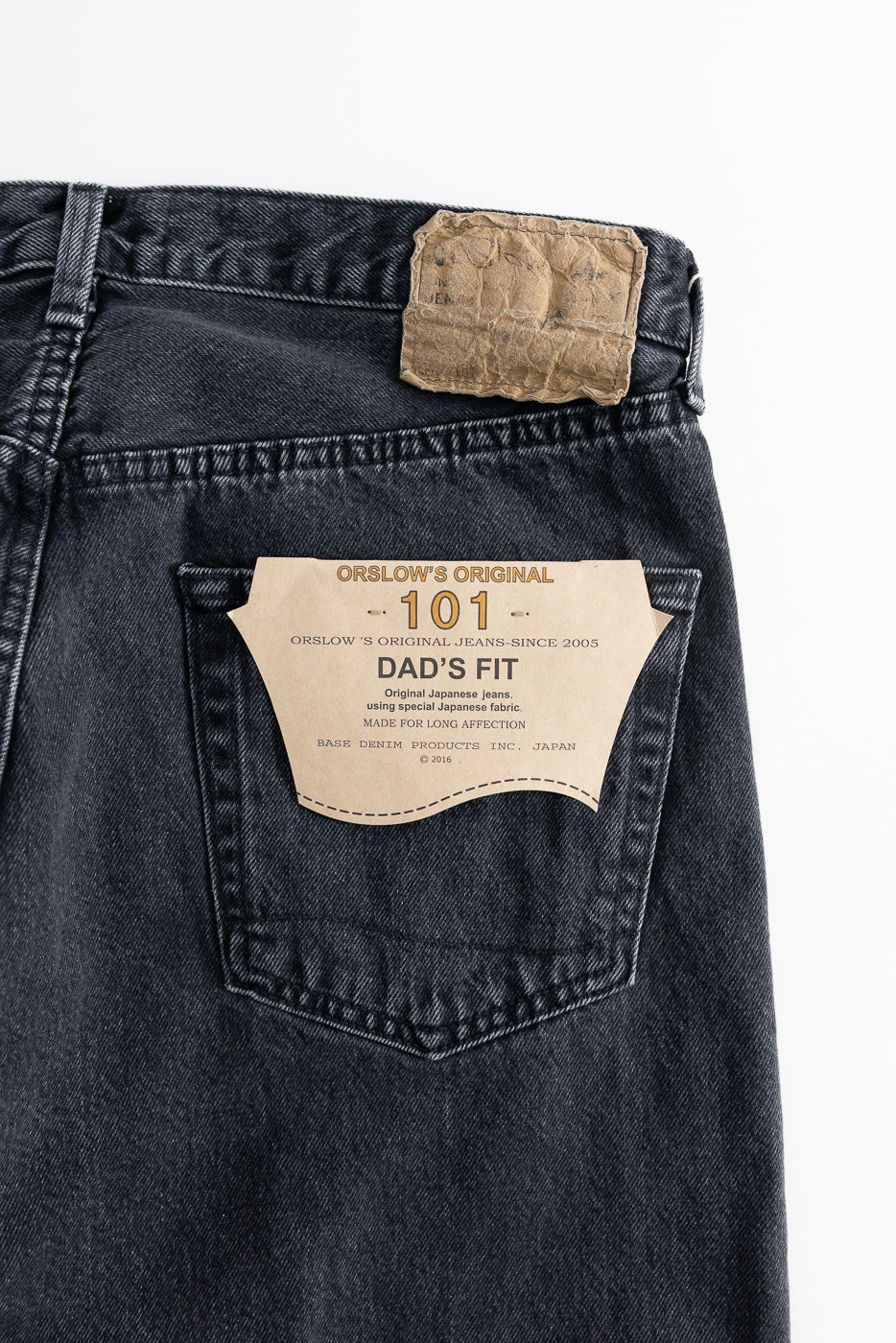 Back view of the 01-1010W-D61S - 101 Dad’s Fit Denim - 90s Black Stone jeans, showcasing the right rear pocket, waistband with belt loops, and a leather patch above a hang-tag detailing the style.