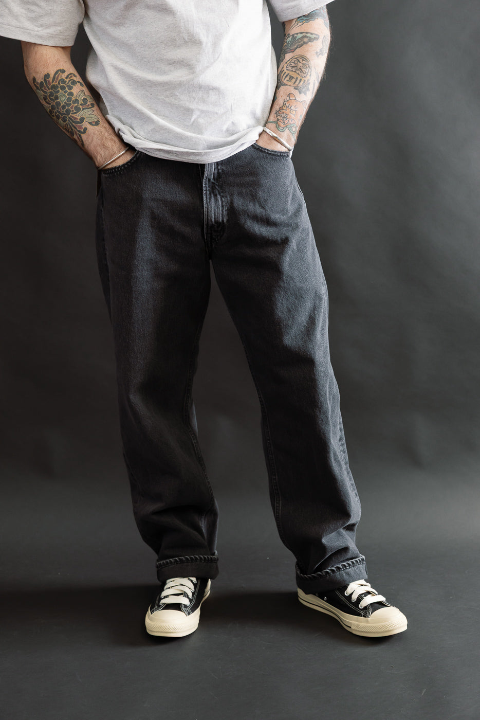 A person models the 01-1010W-D61S - 101 Dad’s Fit Denim - 90s Black Stone, showcasing its relaxed fit and classic five-pocket style, paired with black canvas sneakers.