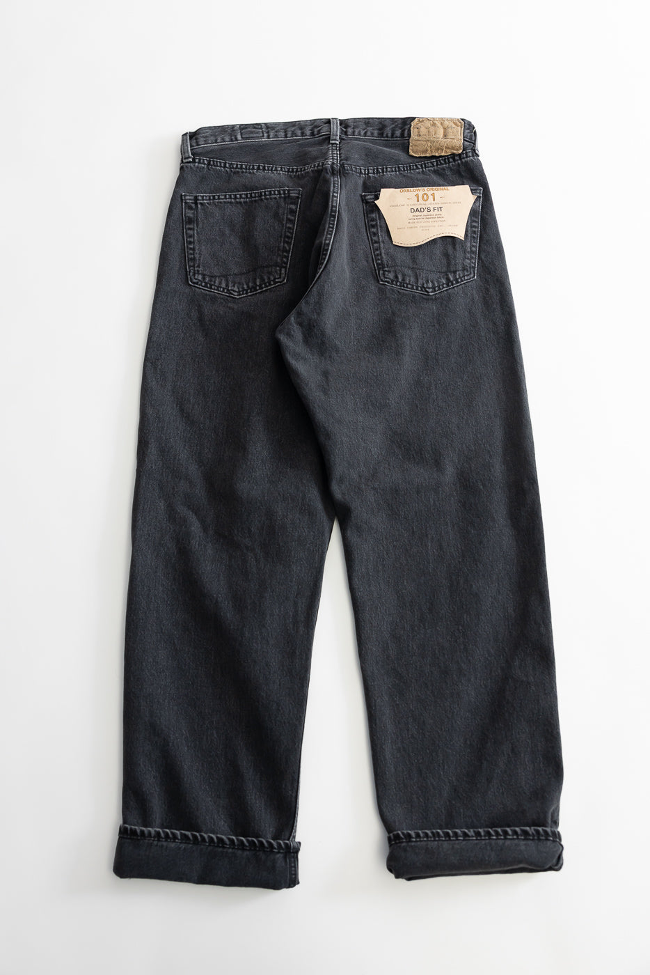 The 01-1010W-D61S - 101 Dad’s Fit Denim - 90s Black Stone showcases black denim jeans, featuring a relaxed fit with rolled cuffs, back pockets, belt loops, leather patch, and a hang-tag reading 101 Dad’s Fit.