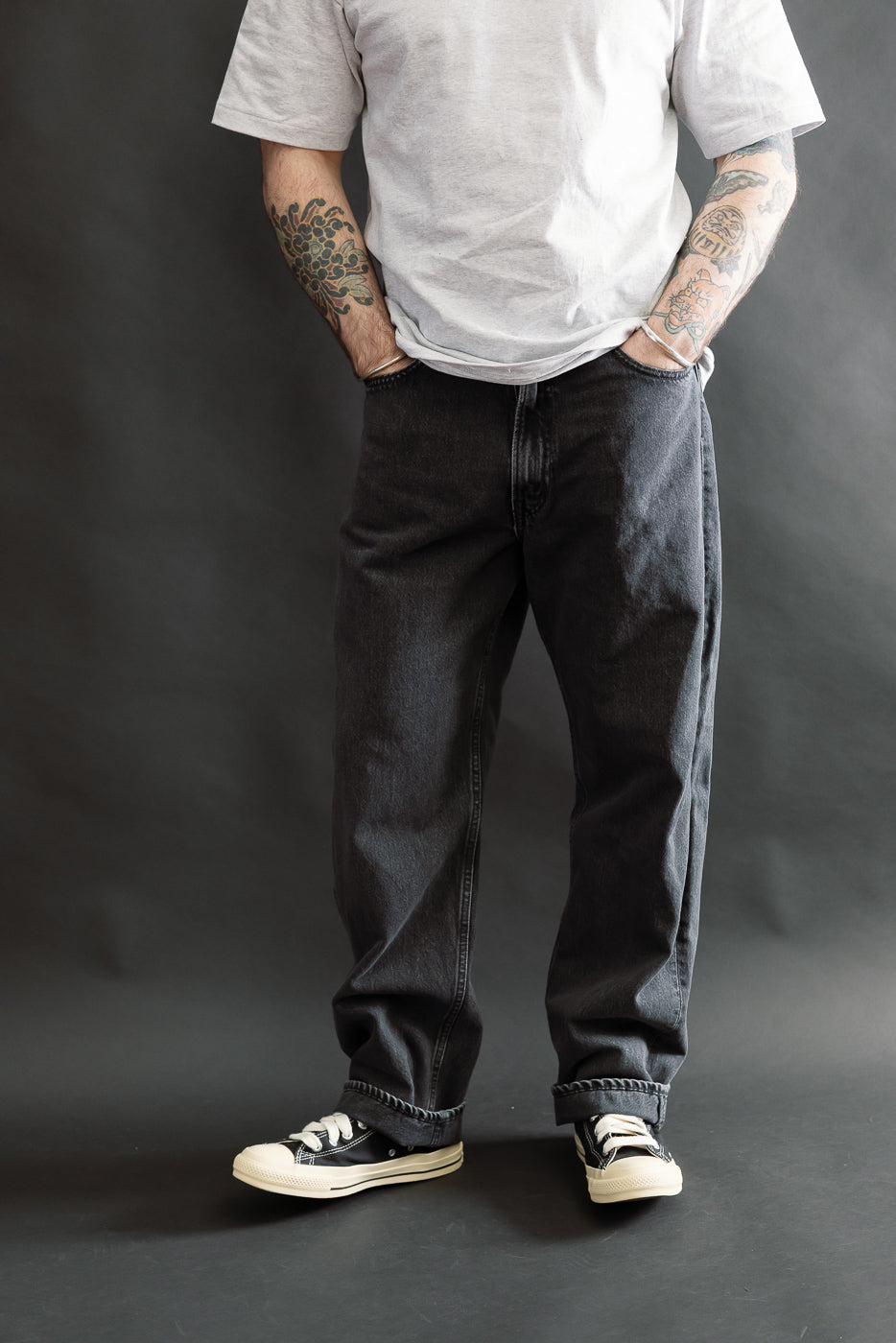Person wearing the 01-1010W-D61S - 101 Dad’s Fit Denim - 90s Black Stone jeans, showcasing a relaxed fit with black stone-washed denim, hands in pockets, styled with casual black canvas sneakers.