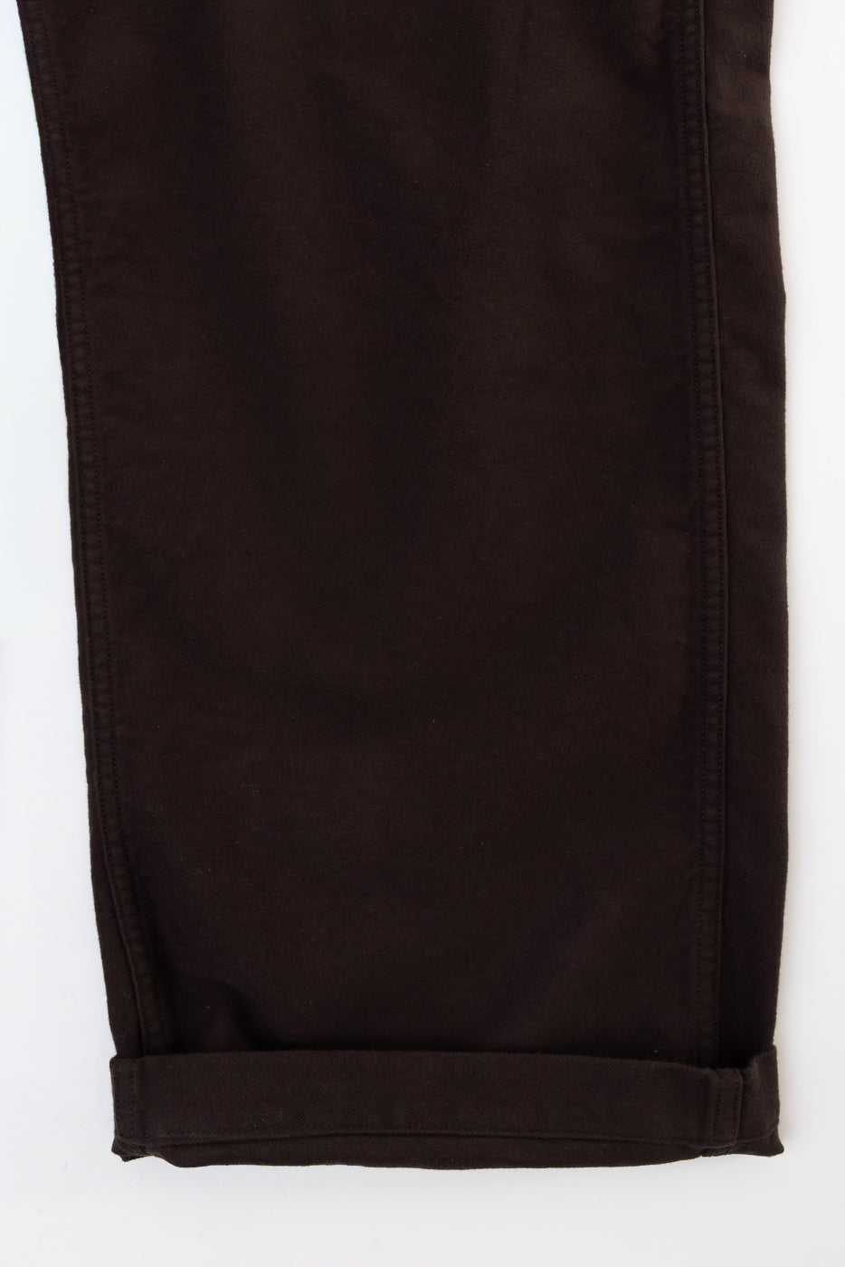 Close-up of the bottom hem and rolled cuff of dark brown cotton trousers, front view.
