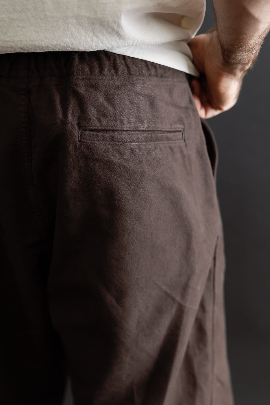 Close-up back view of brown casual trousers showing rear welt pocket detail.