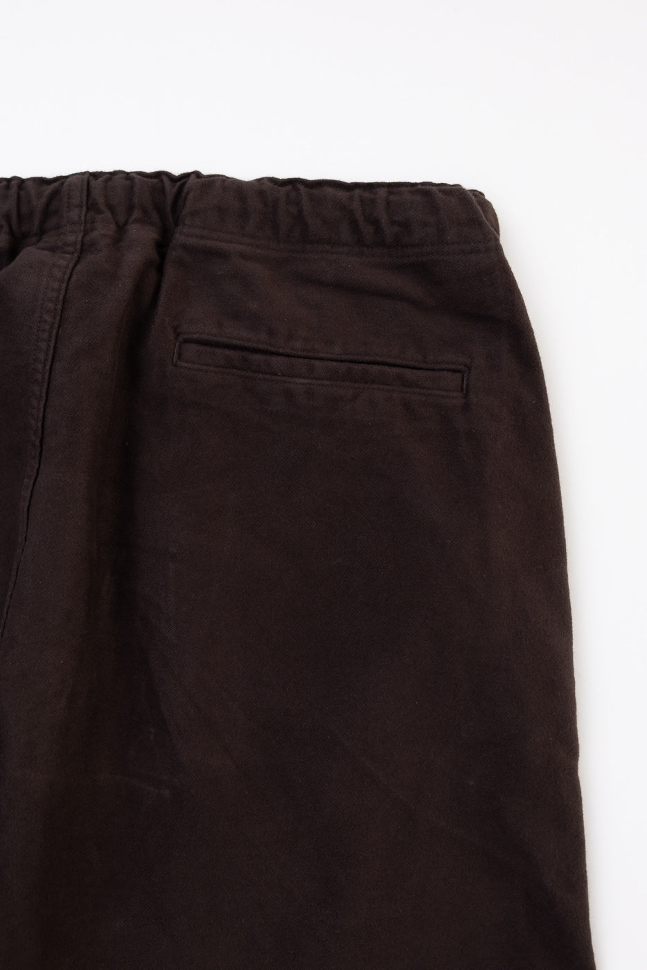 Close-up flat lay showing the back left pocket and elastic waistband of dark brown trousers.