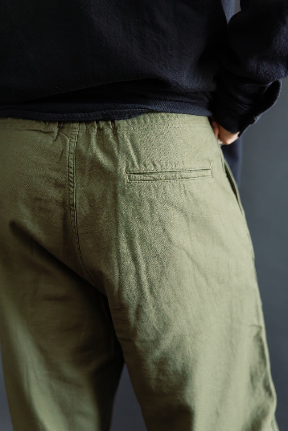 Close-up of male model's back right side wearing orSlow dark olive wide fit New Yorker pants, showing rear pocket detail.