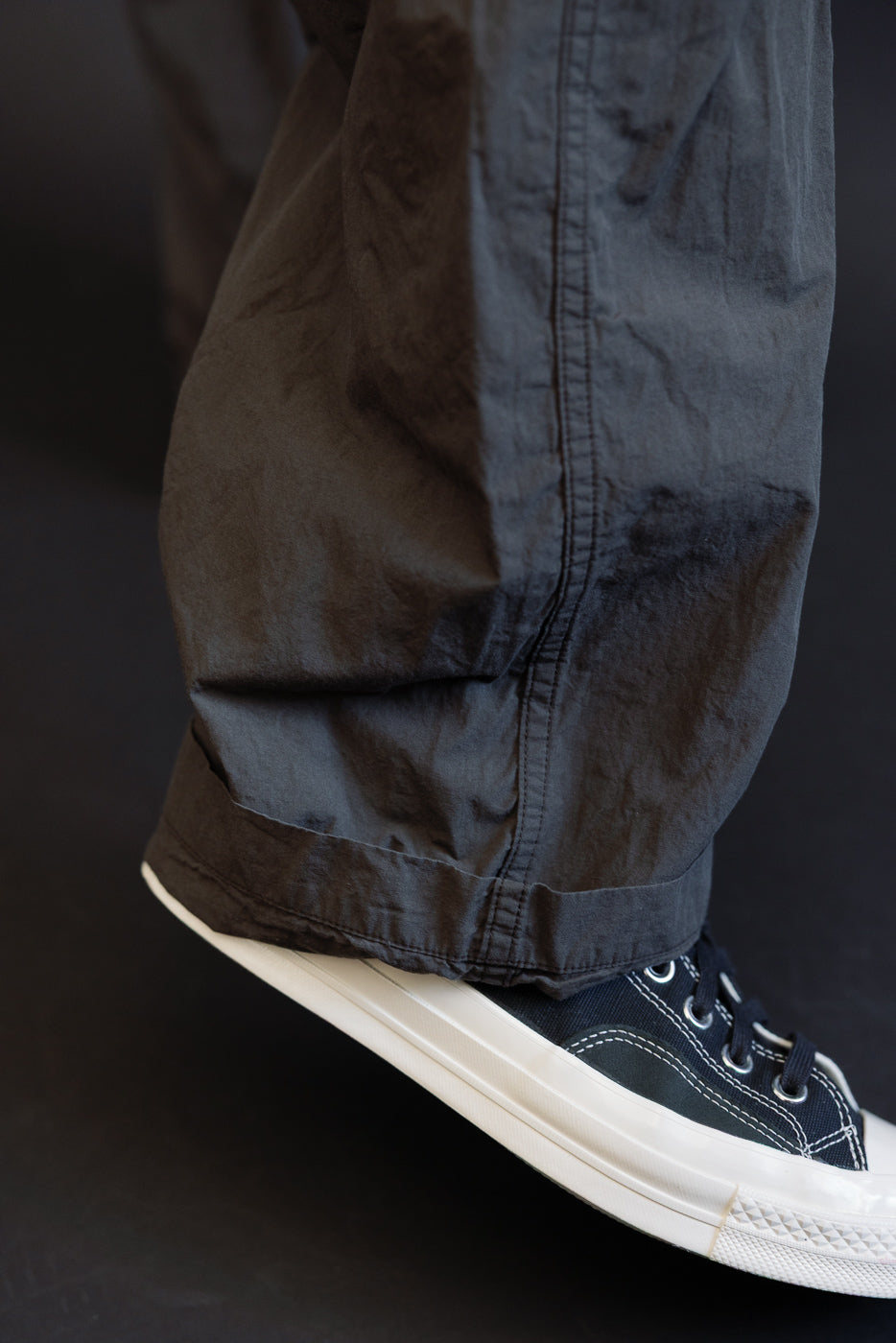 Close-up side view of male model's dark cargo pants hem with cuffed detail, paired with navy sneakers