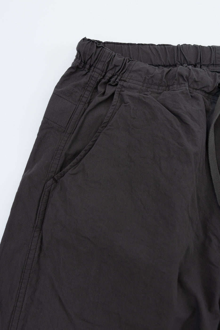 Close-up front view of black drawstring waist pants, elastic waistband, side seam detail