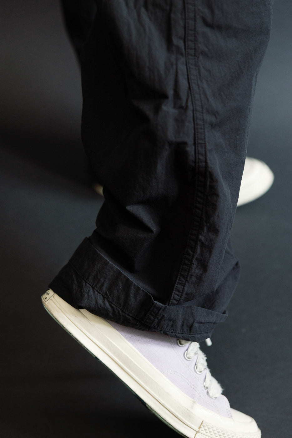 Close-up side view of male model’s black cargo pants hem, cuffed over light purple sneakers, athletic build