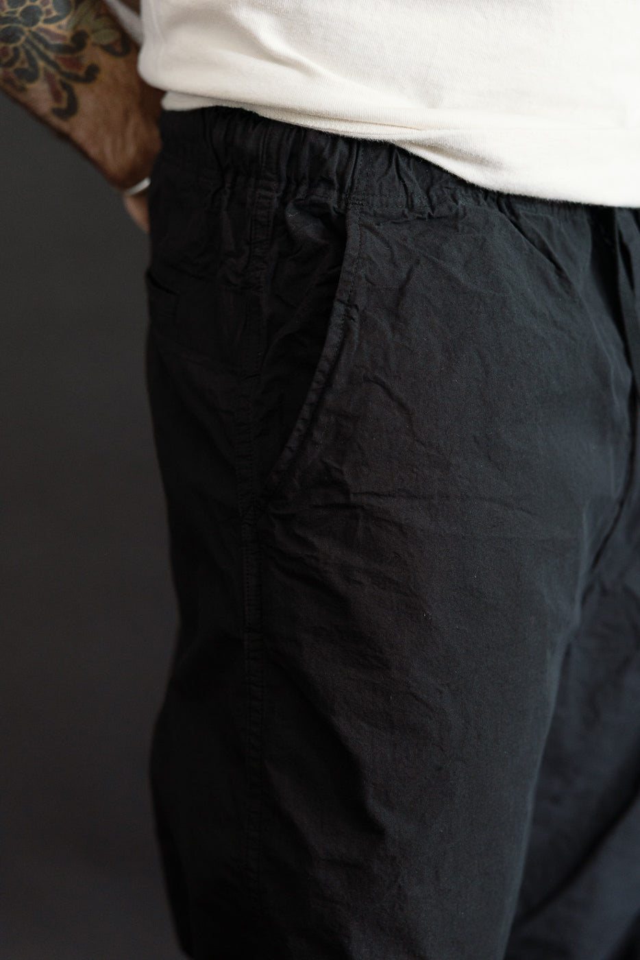 Close-up side view of black casual pants with elastic waist, worn by male model, 5'9
