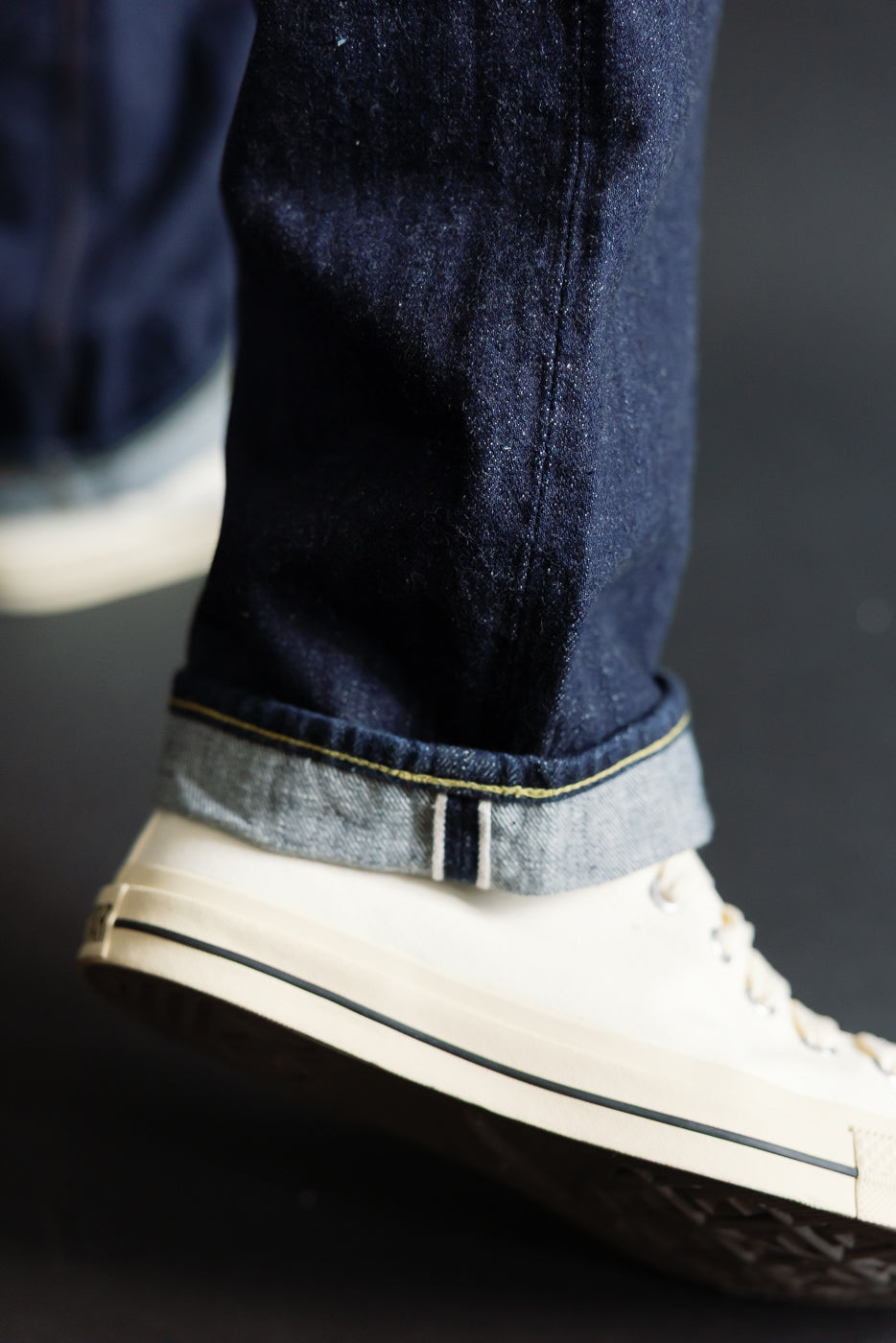 Close-up of men's selvedge denim jeans cuff and hem, showing front leg detail with white sneaker.