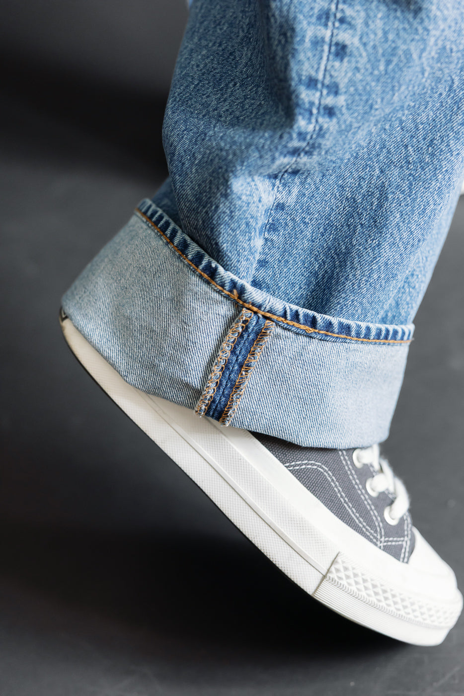 Close-up of the cuffed bottom hem of blue denim jeans worn with grey canvas sneakers.