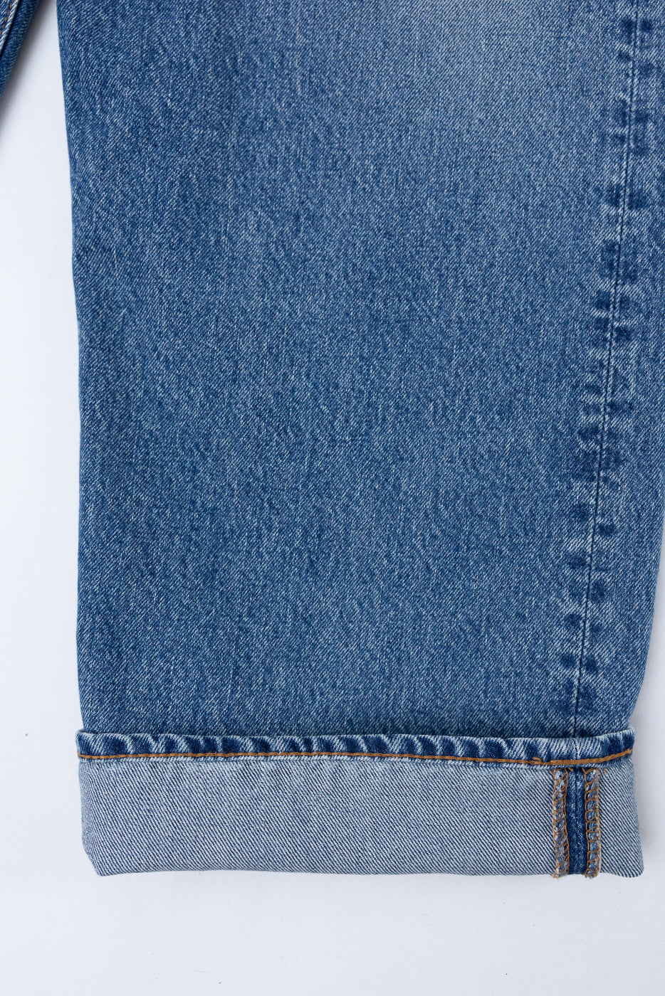 Close-up of the bottom hem and rolled cuff of the front of blue denim jeans.