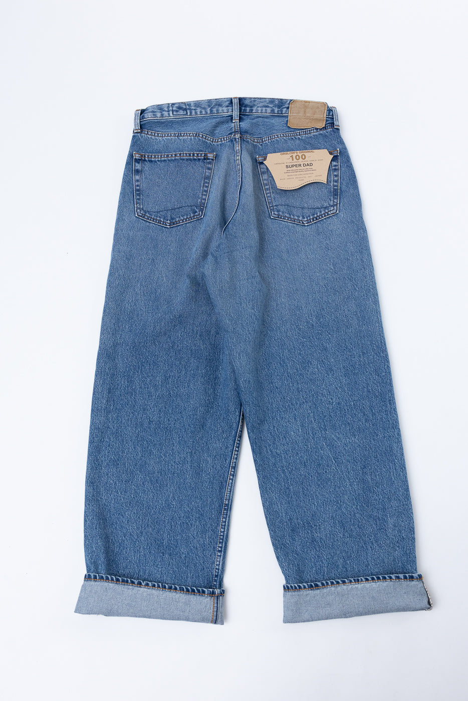 Back view flat lay of blue denim jeans with a leather patch and '100 SUPER DAD' tag.