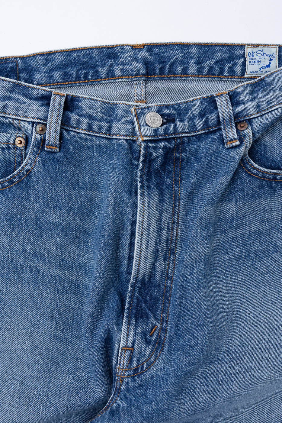 Close-up front view of blue denim jeans showing waistband, button fly, and pocket details.