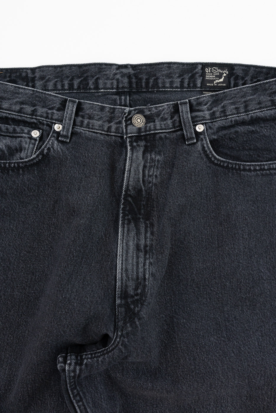 Close-up front of dark selvedge denim jeans, showing button fly, belt loops, and Orslow brand tag, made in Japan
