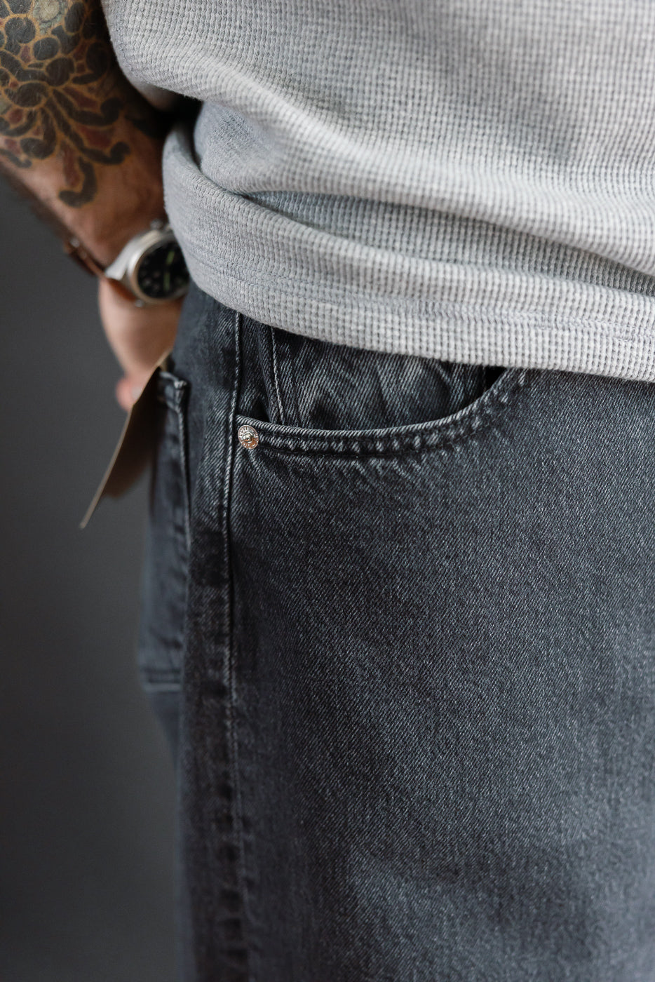 Close-up of front right pocket on charcoal jeans worn by male model, 5'9