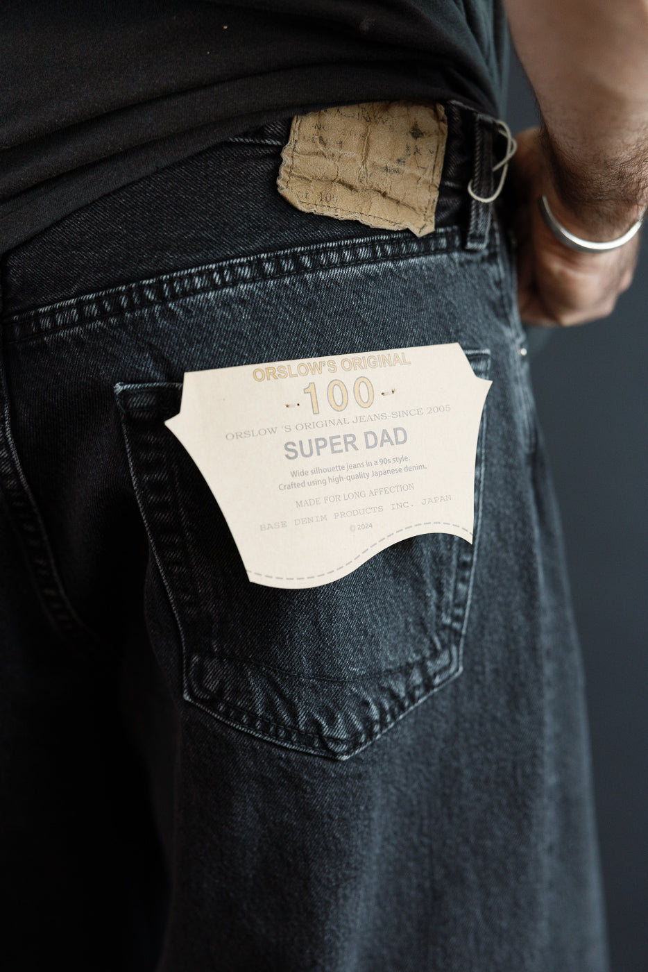 Close-up back view of male model wearing Orslow 100 Super Dad jeans, showing rear pocket tag and selvedge denim texture