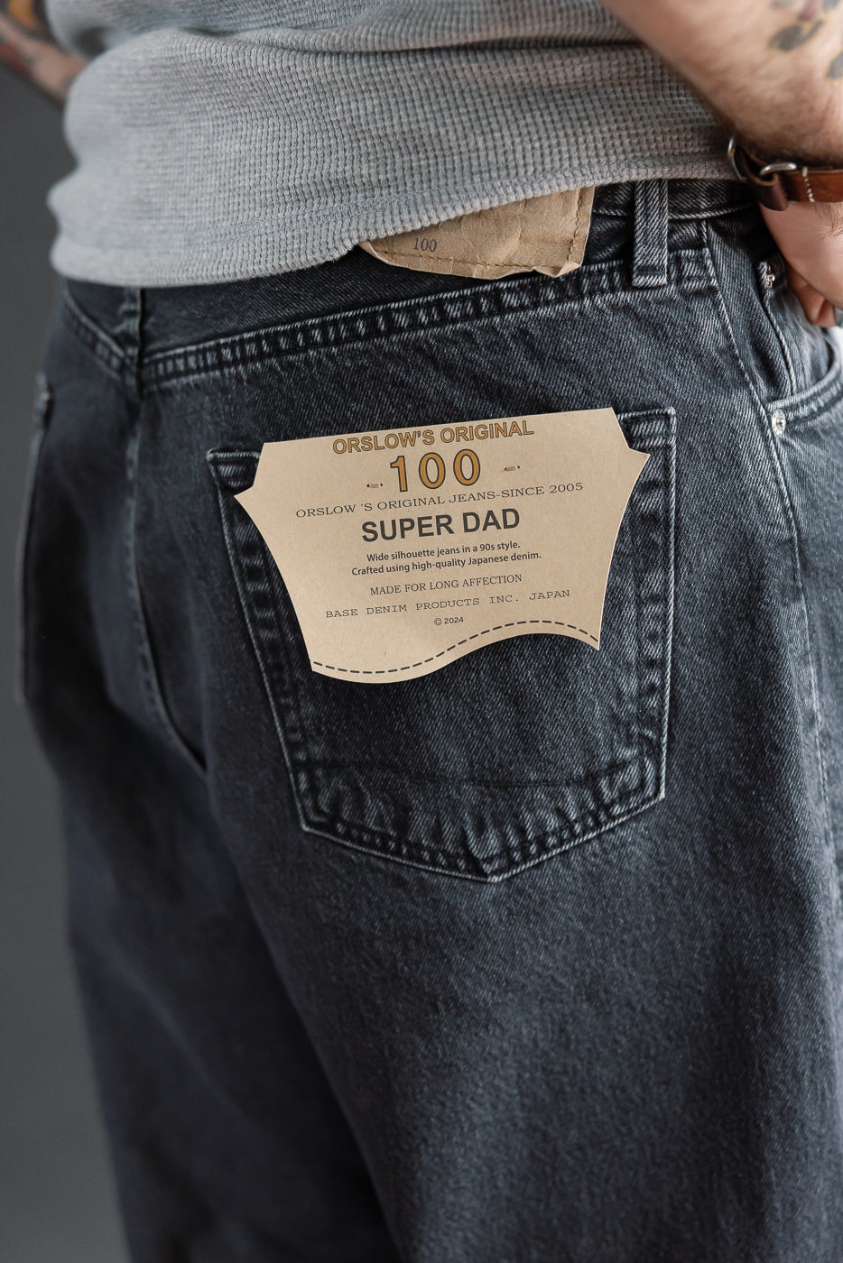 Close-up of the back right pocket of black denim jeans featuring a tan Orslow Super Dad patch.