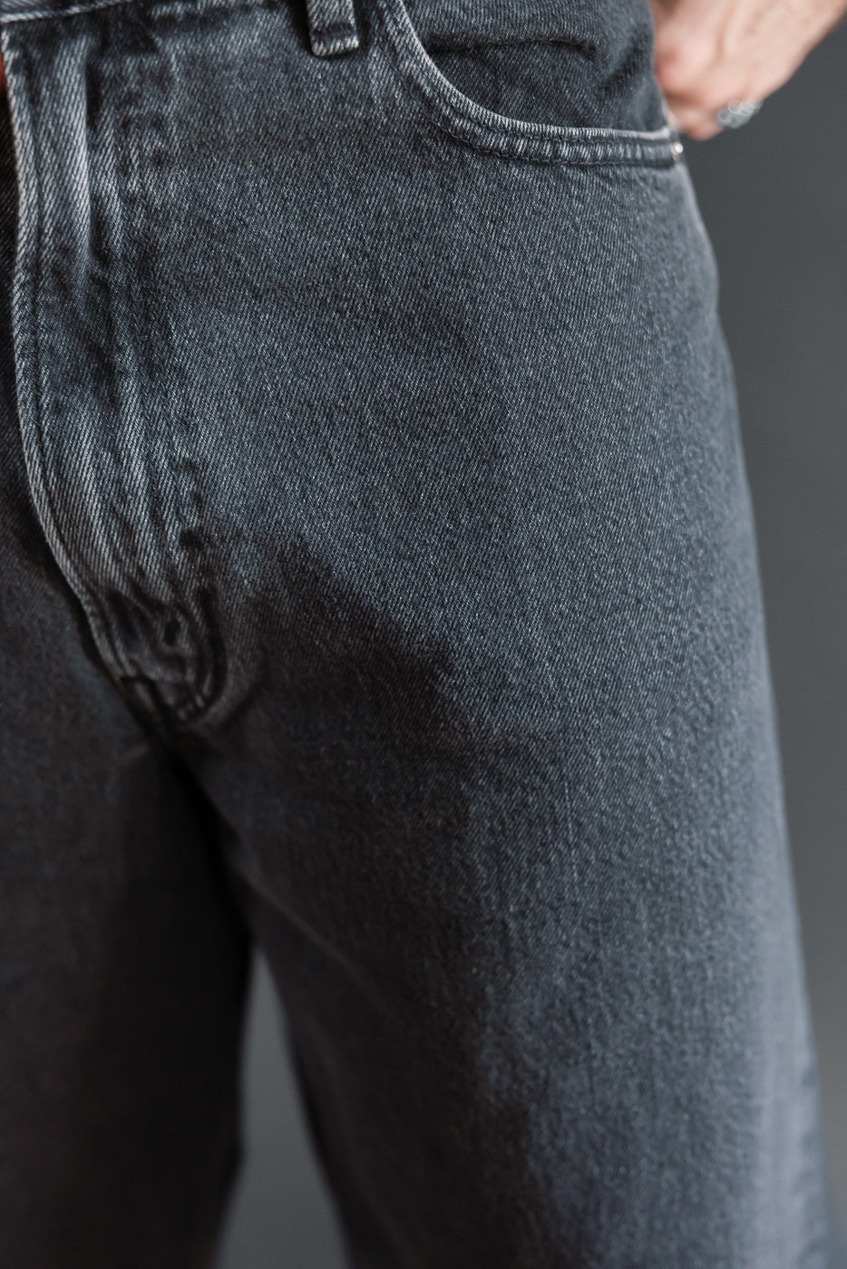 Close-up of the front of a male model's dark grey selvedge denim jeans, showing fabric texture.