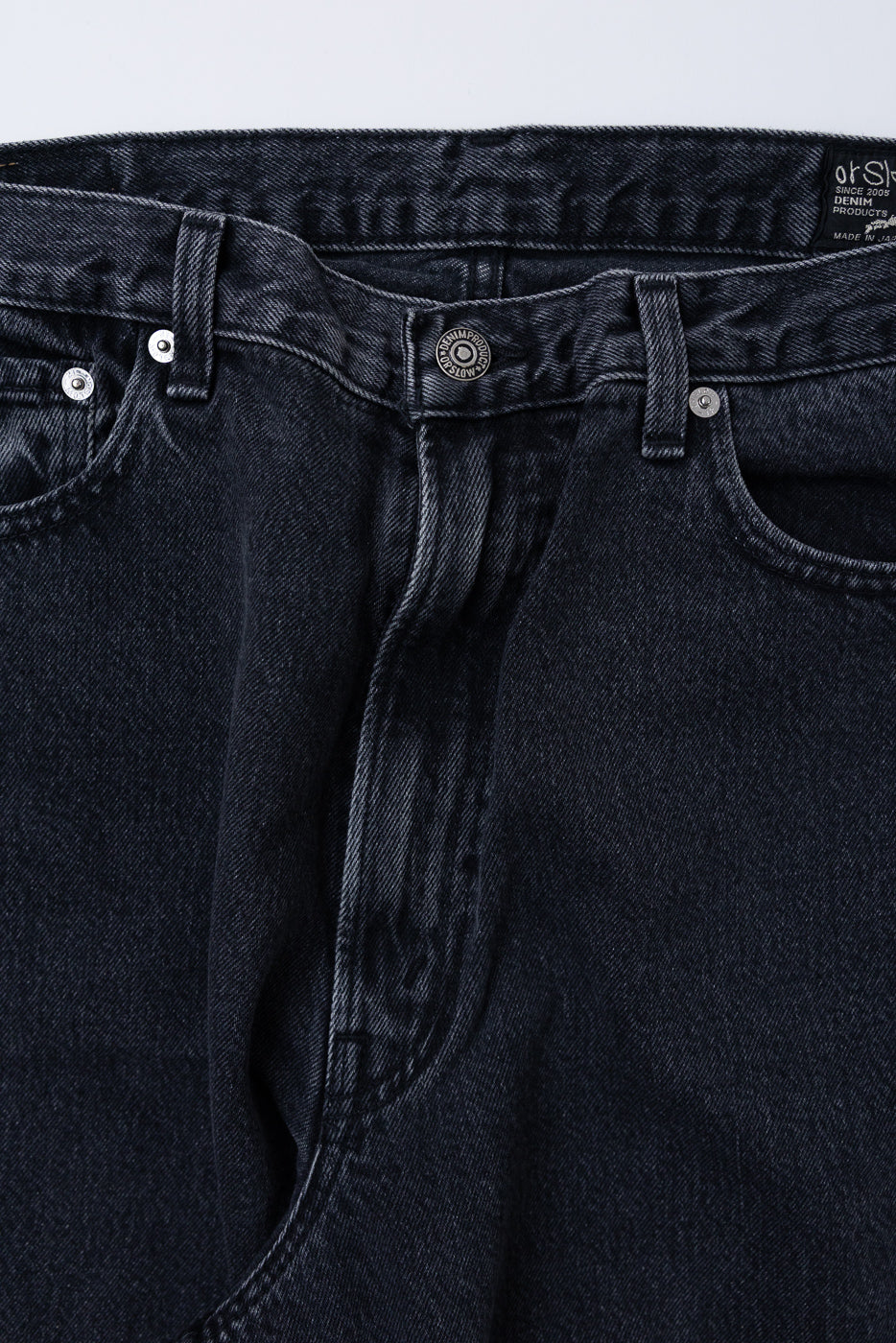 Close-up front view of black denim jeans showing waistband, button, and belt loops.