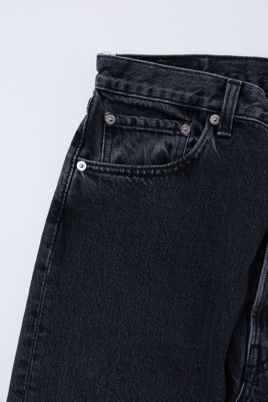 Close-up of the front waist and pocket of black denim jeans, showing metal rivets and texture.
