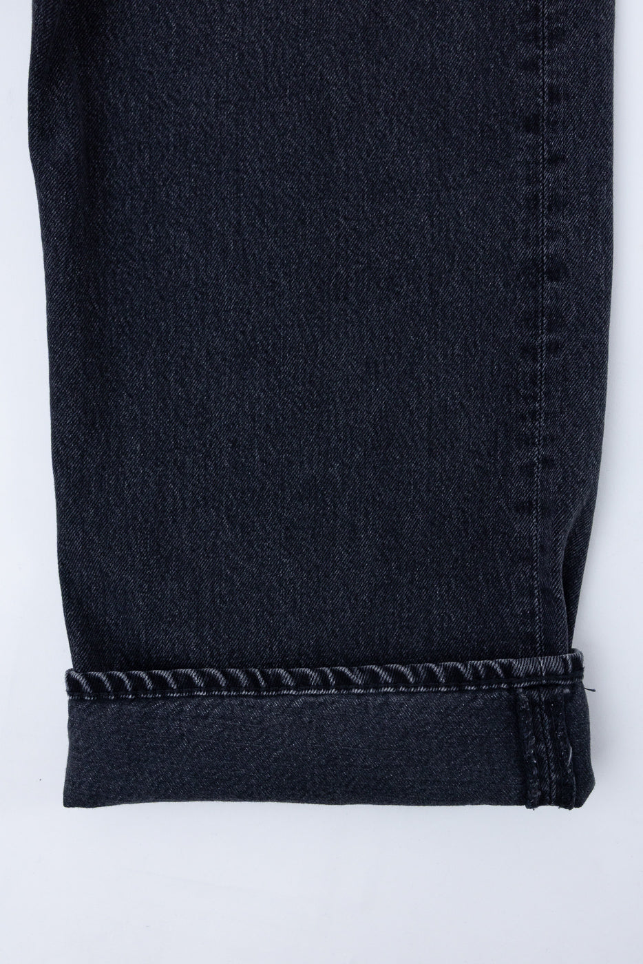 Close-up of the bottom hem and selvedge detail on the front of dark indigo denim jeans.