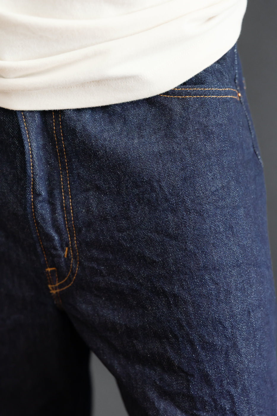 Close-up front view of dark indigo selvedge denim jeans showing fabric texture and stitching.